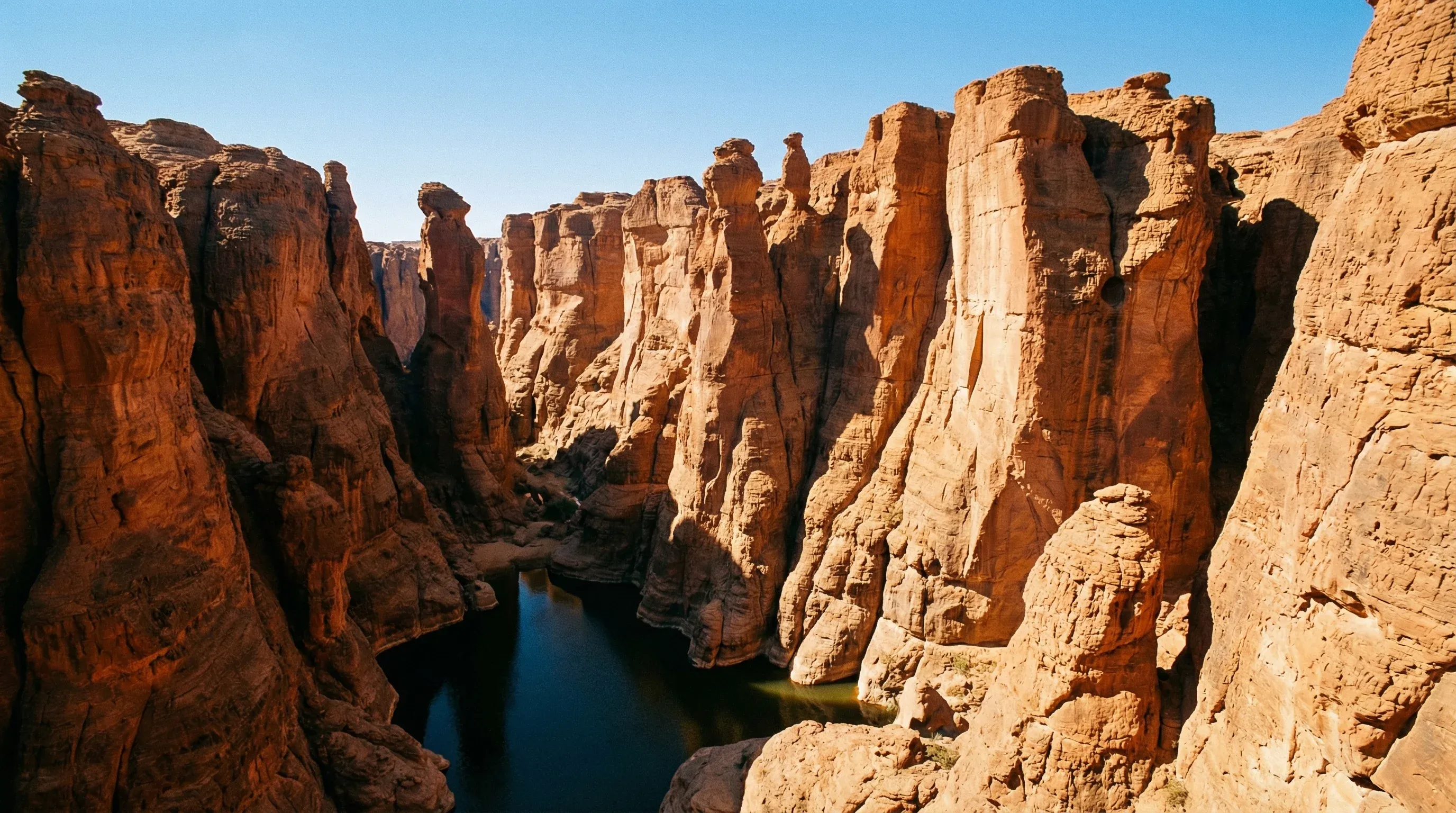 Deep orange sandstone cliffs surrounding the dark water of the Guelta d’Archei canyon in the Ennedi Massif of northern Chad.