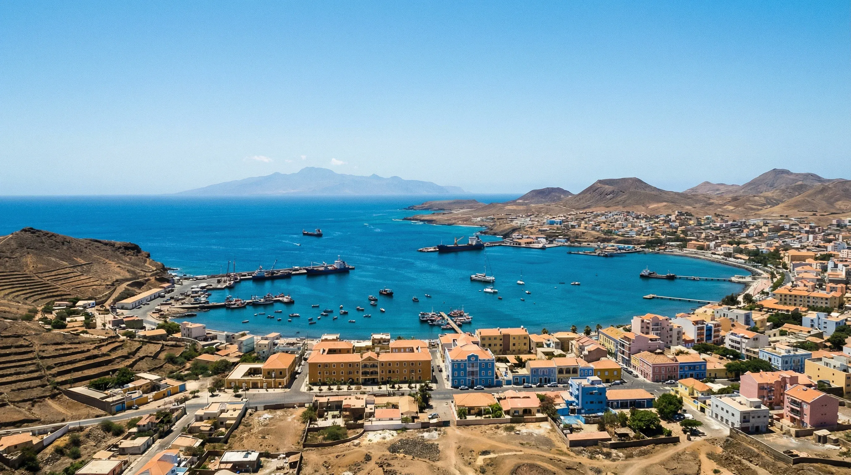 A high-altitude view of the crescent-shaped Mindelo Bay and the surrounding volcanic landscape under a clear sky in São Vicente.