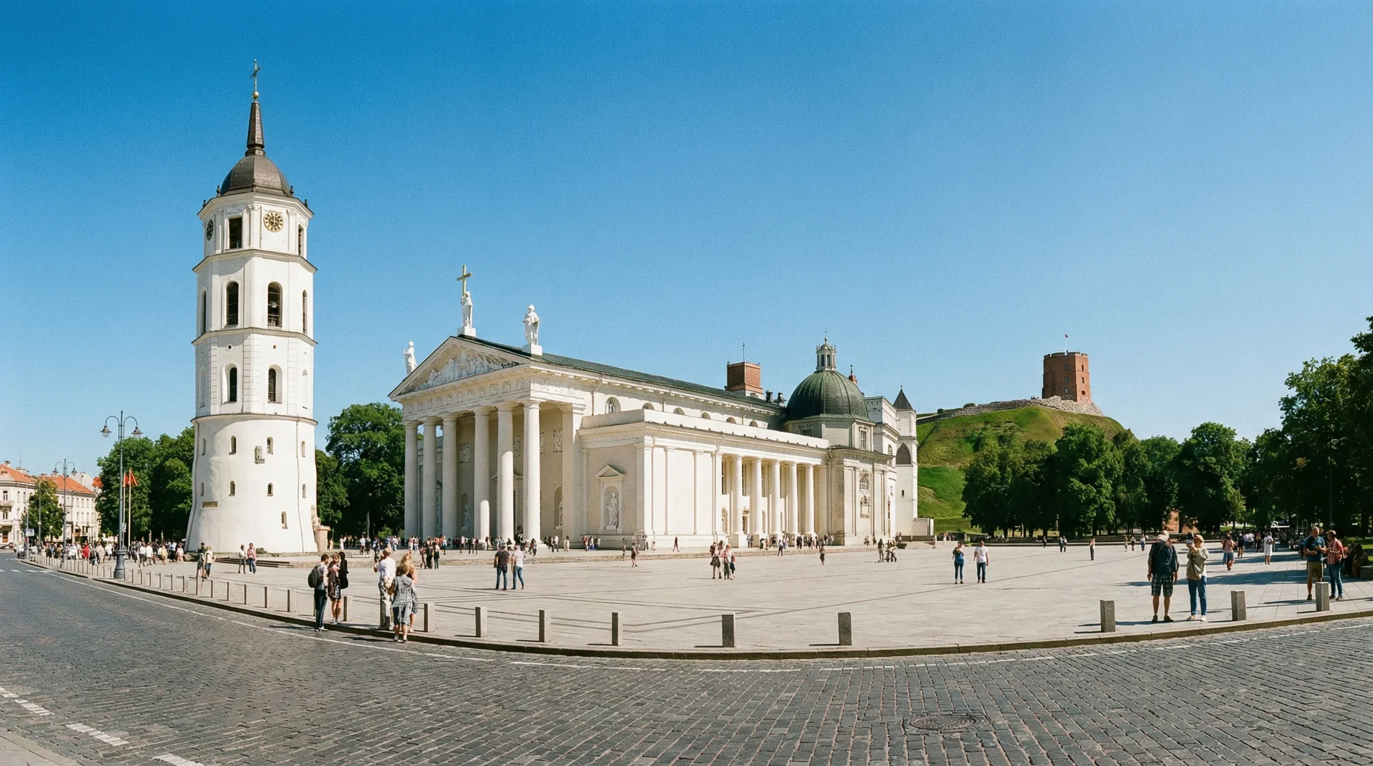 Vilnius Cathedral and its separate white bell tower in Cathedral Square under a clear blue sky at midday.