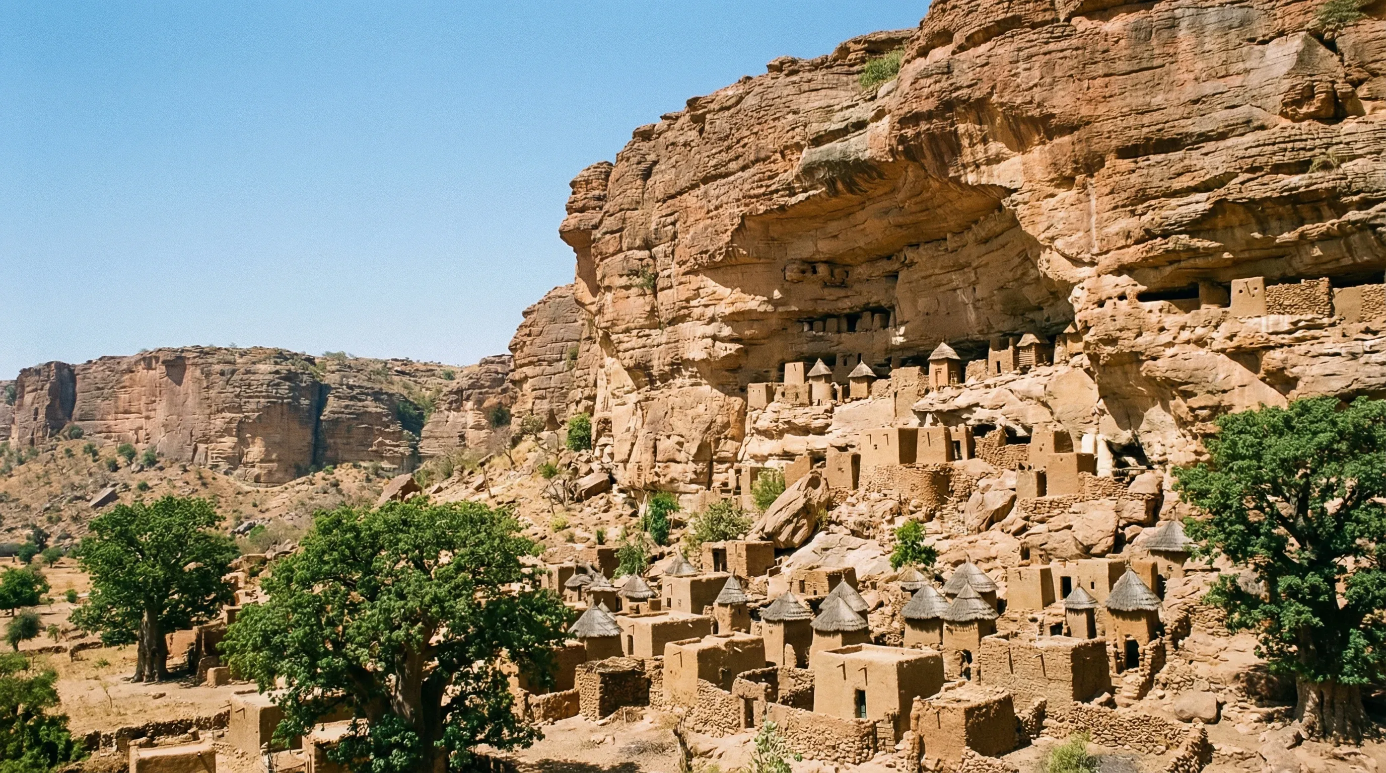 Traditional Dogon village houses with conical straw roofs built along the base of the Bandiagara Escarpment cliffs in Mali.