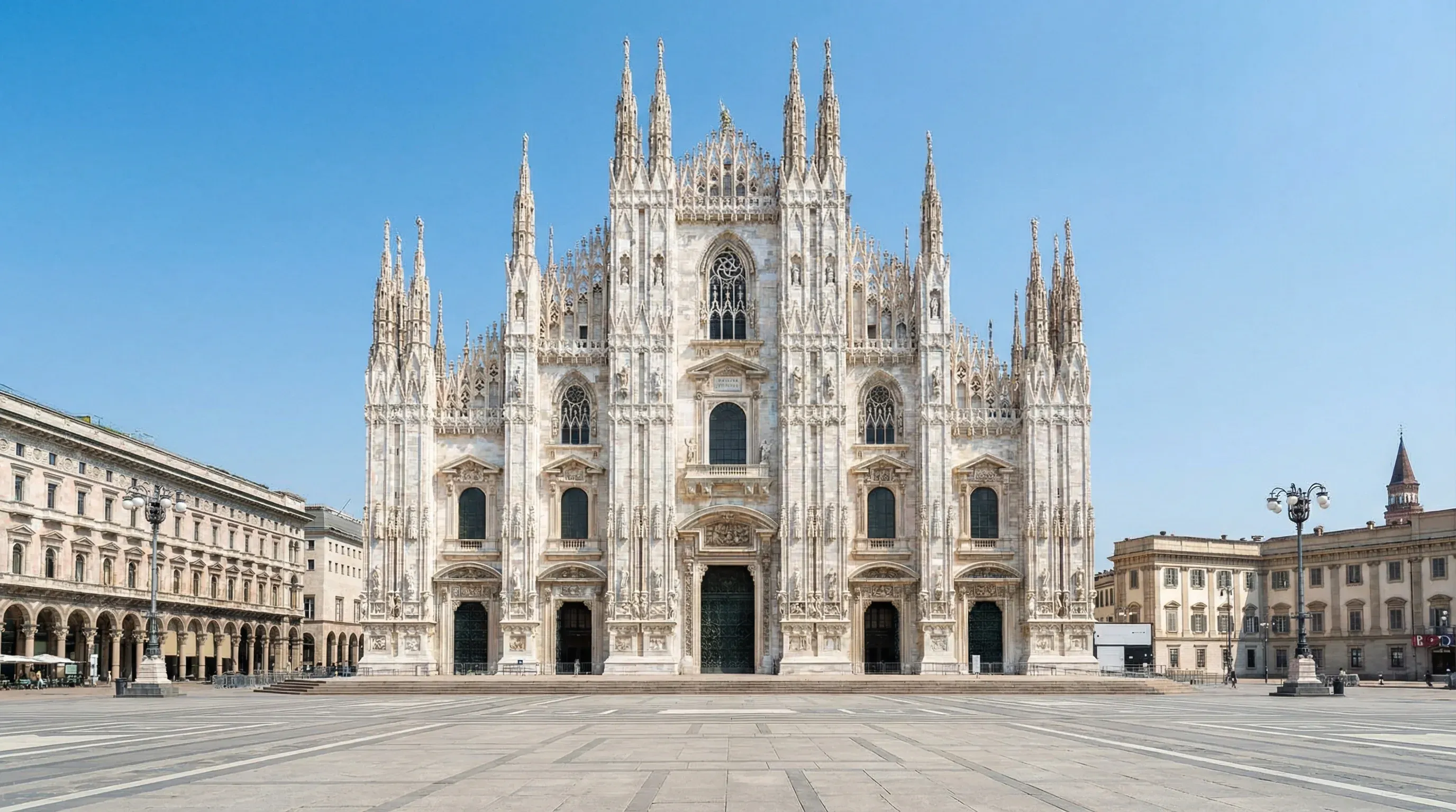 The white marble Gothic facade and spires of the Milan Cathedral under a bright midday sun.