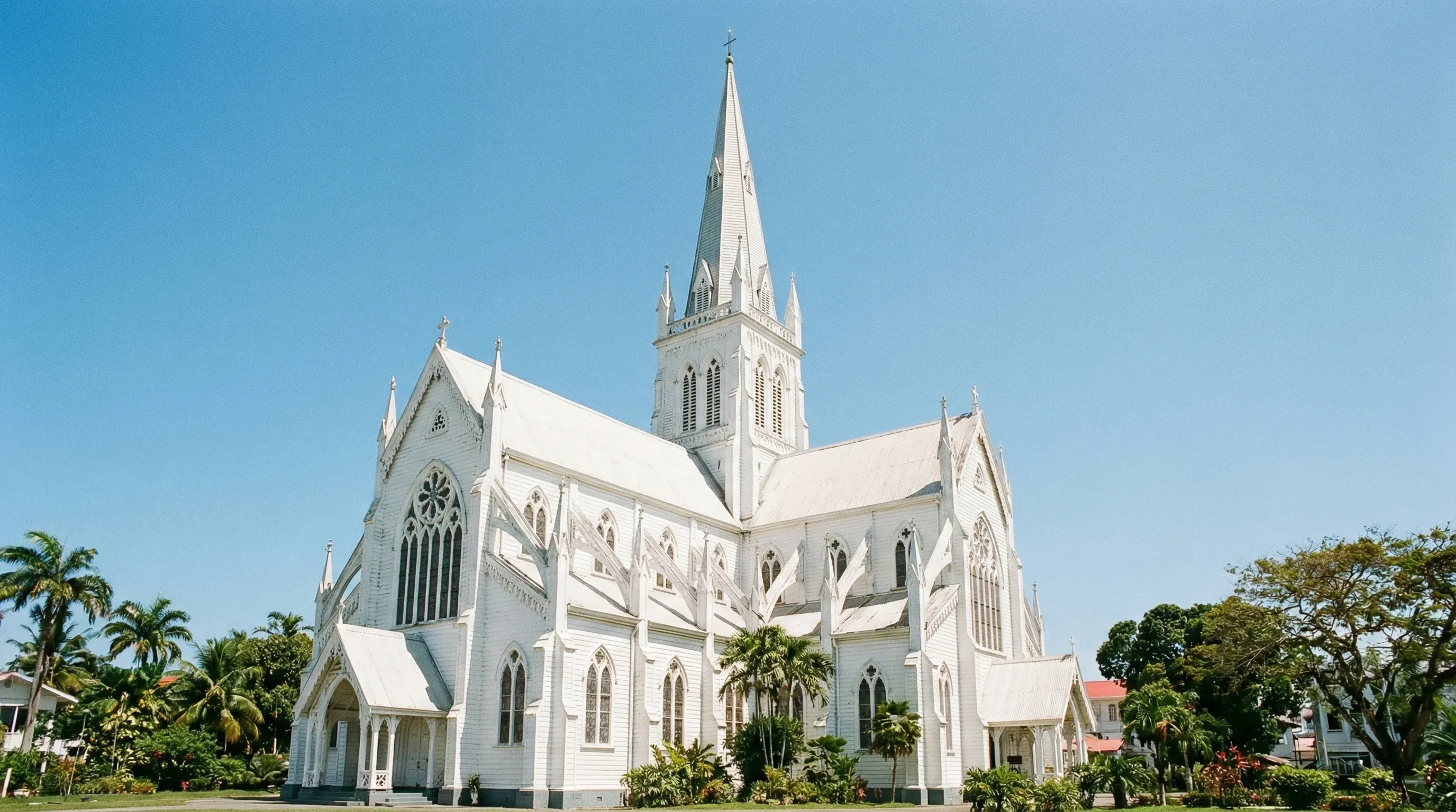 A wide-angle view of the white wooden St. George's Cathedral in Georgetown, Guyana, under a clear blue sky.
