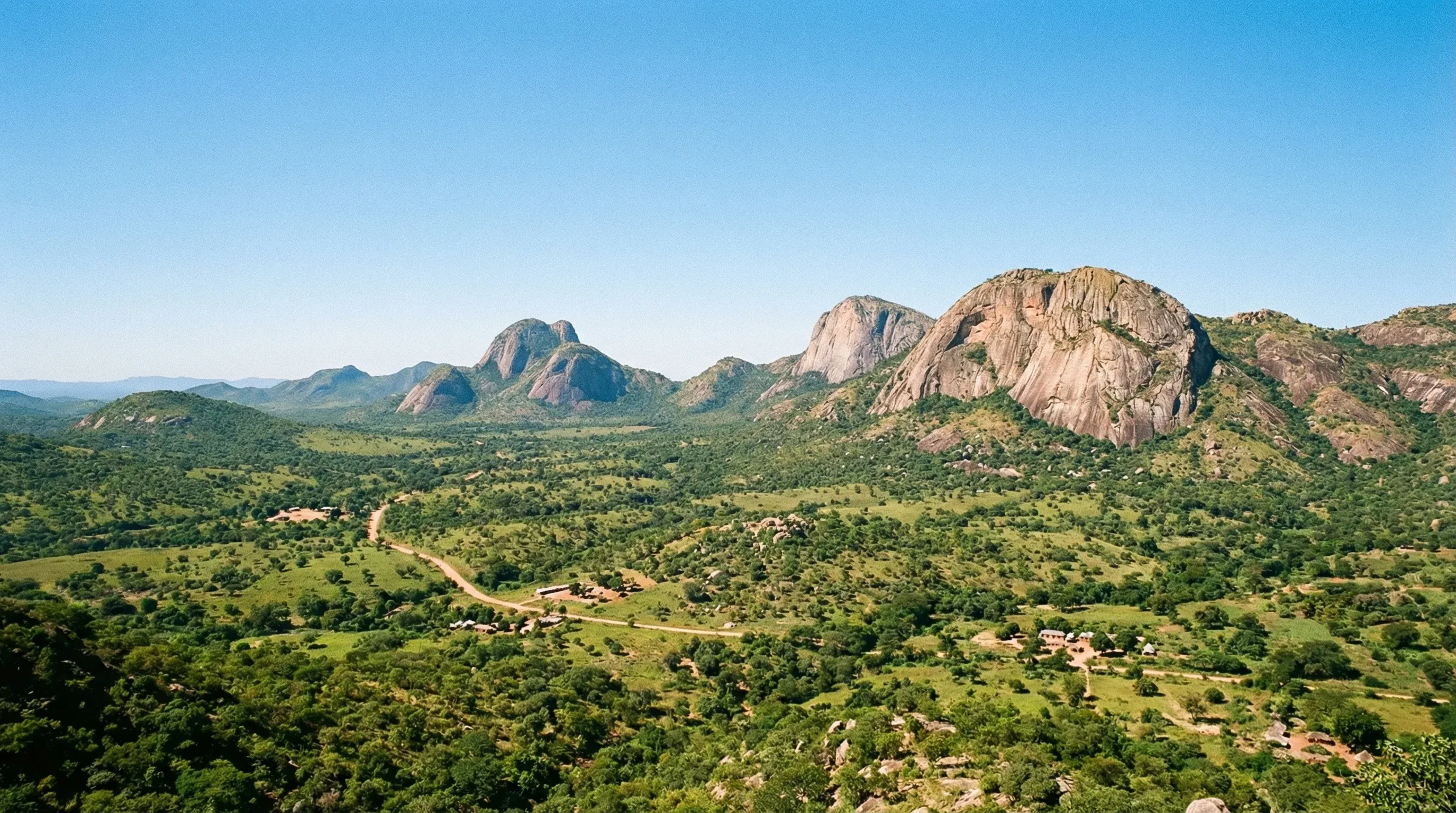 A wide landscape view of the green hills and granite inselbergs of the Chongoni Rock Art Area in central Malawi under a clear blue sky.