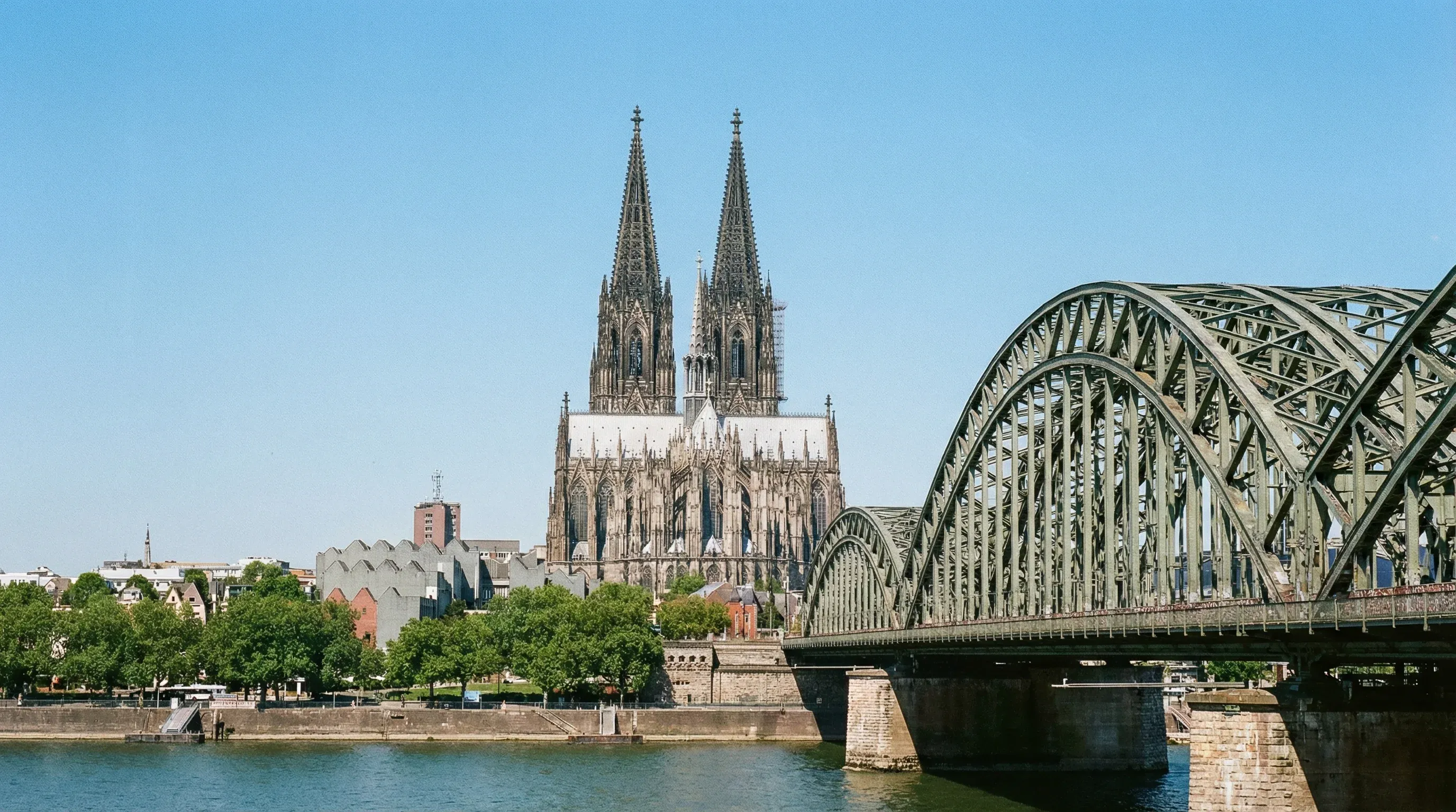 The twin spires of Cologne Cathedral rise behind the steel arches of the Hohenzollern Bridge over the Rhine.