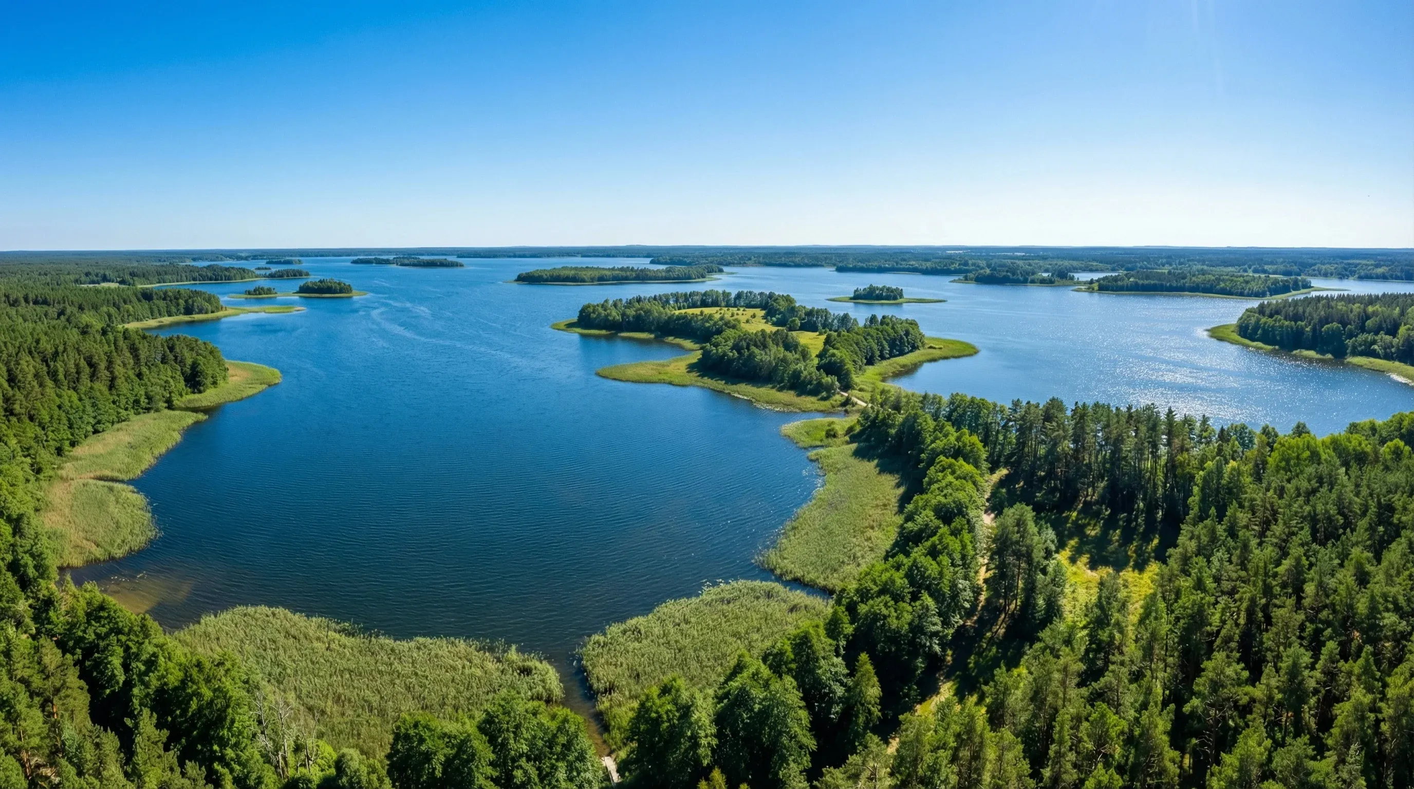 An elevated panoramic view of the blue Braslav Lakes with green islands and dense forests under a clear sky.