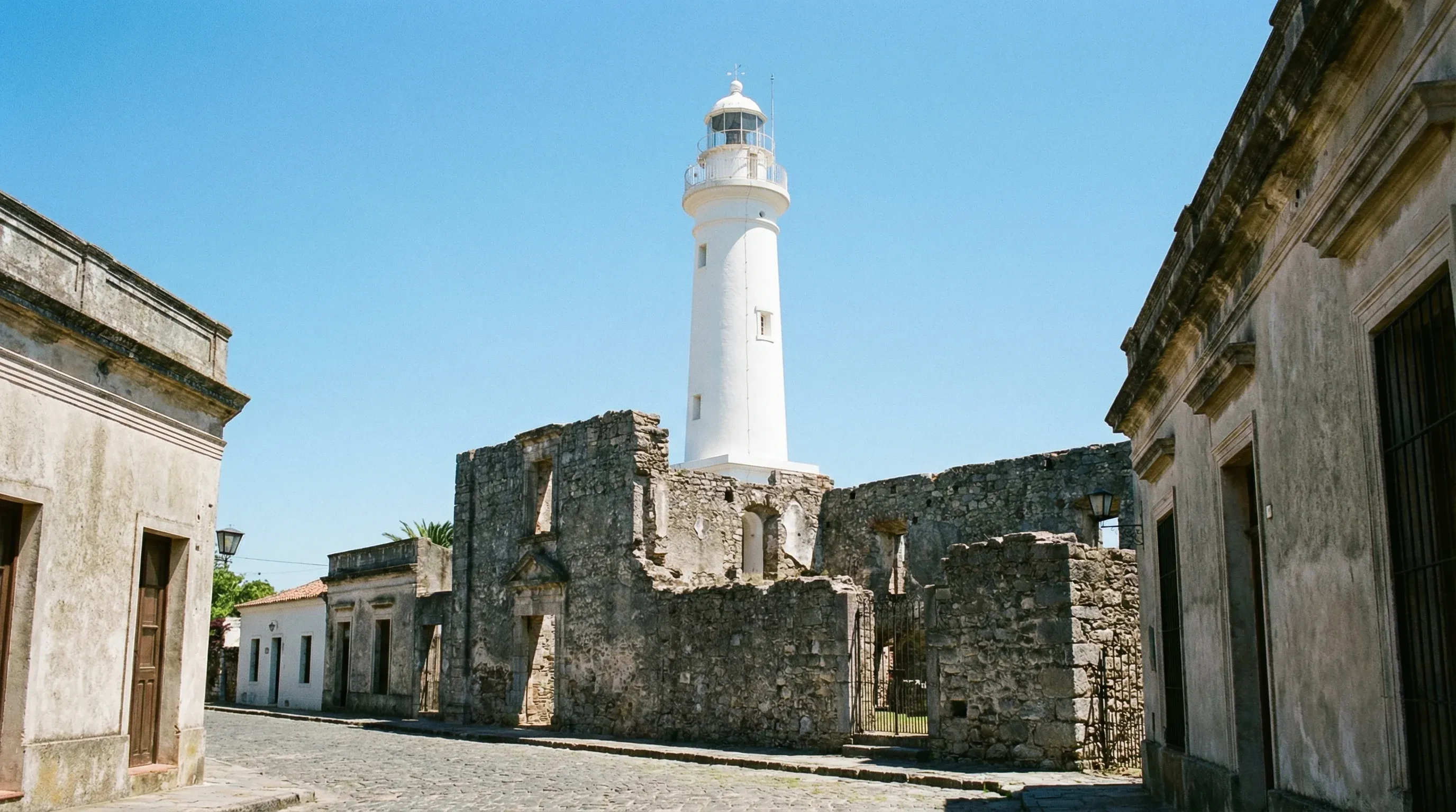 A white 19th-century lighthouse stands next to the stone ruins of an ancient convent under a clear blue sky in the historic quarter of Colonia del Sacramento.