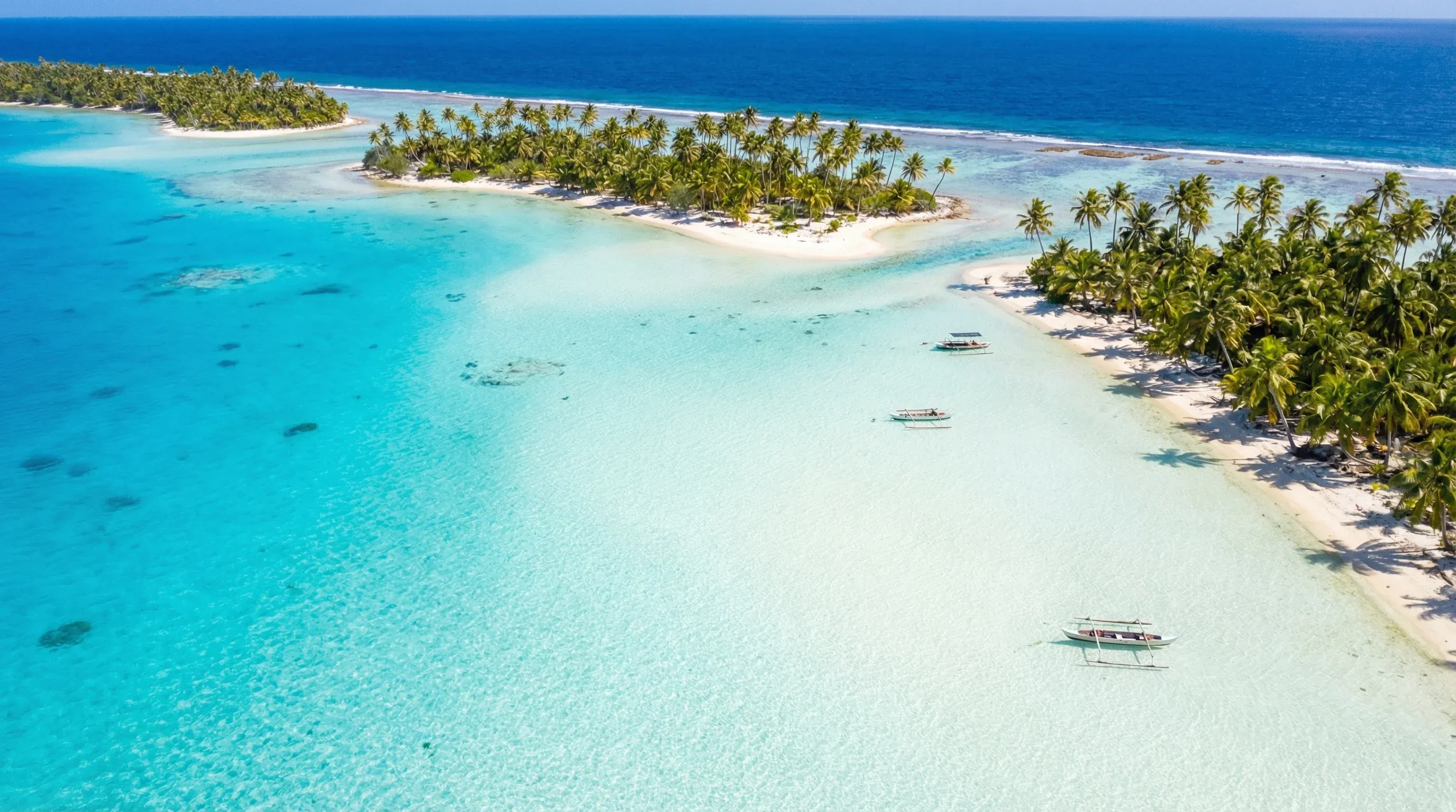 Shallow turquoise water surrounds small sandy islands with palm trees at the Blue Lagoon in Rangiroa Atoll.