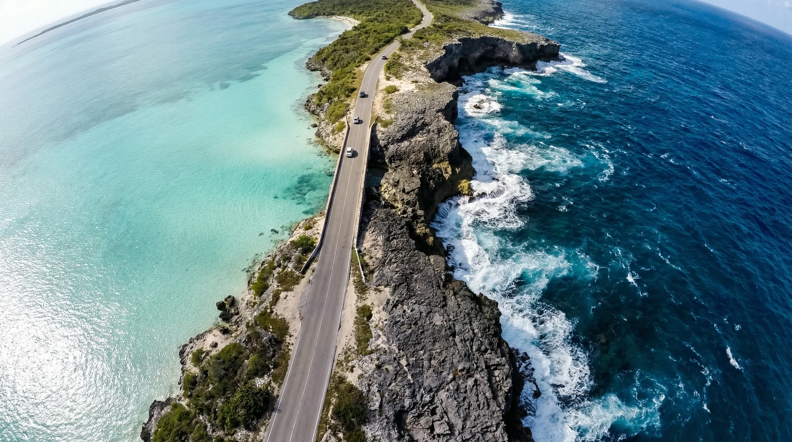 A high-angle view of the Glass Window Bridge in Eleuthera, separating the dark Atlantic Ocean from the light turquoise Bight.