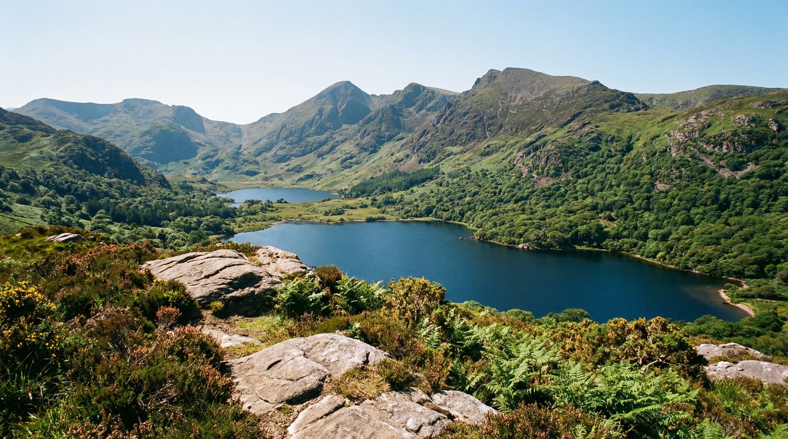 A wide landscape view over a series of blue lakes and green forested mountains in Killarney National Park from an elevated viewpoint.