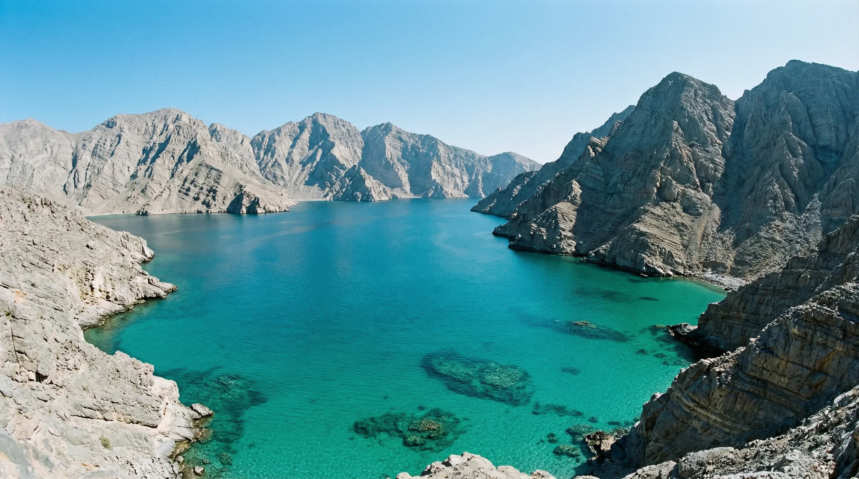 Steep limestone mountains overlooking the deep turquoise waters of the Khor Sham fjord in the Musandam Peninsula.