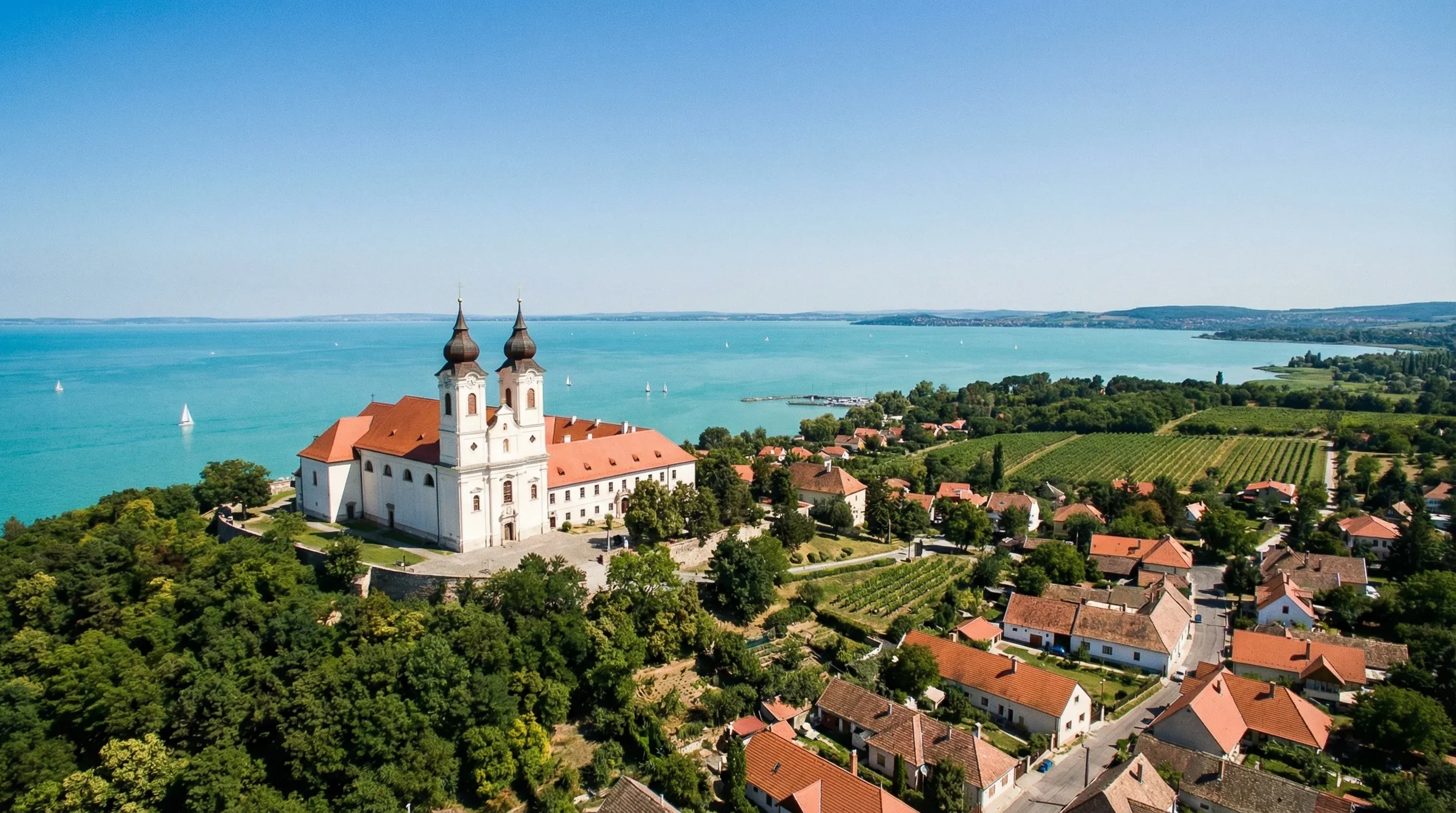 A white abbey with two towers on a hill overlooking the expansive blue waters of Lake Balaton.