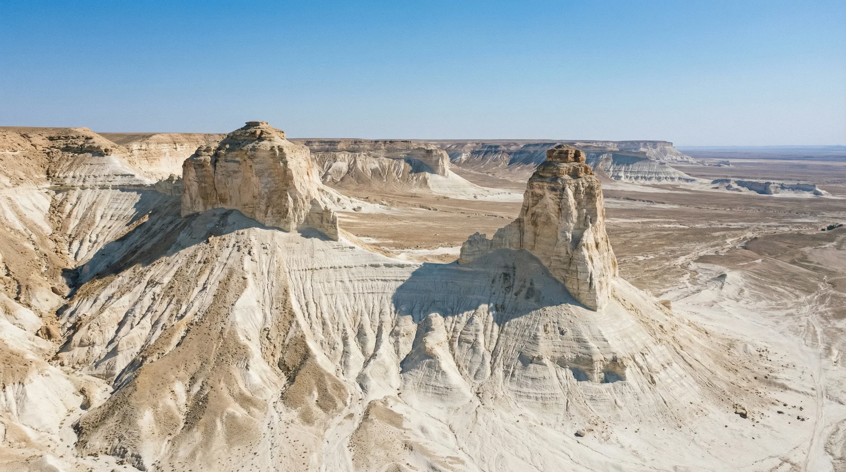 A wide-angle view of the Bozzhira Tract's white limestone peaks rising from a desert plateau in the Mangystau Region of Kazakhstan.