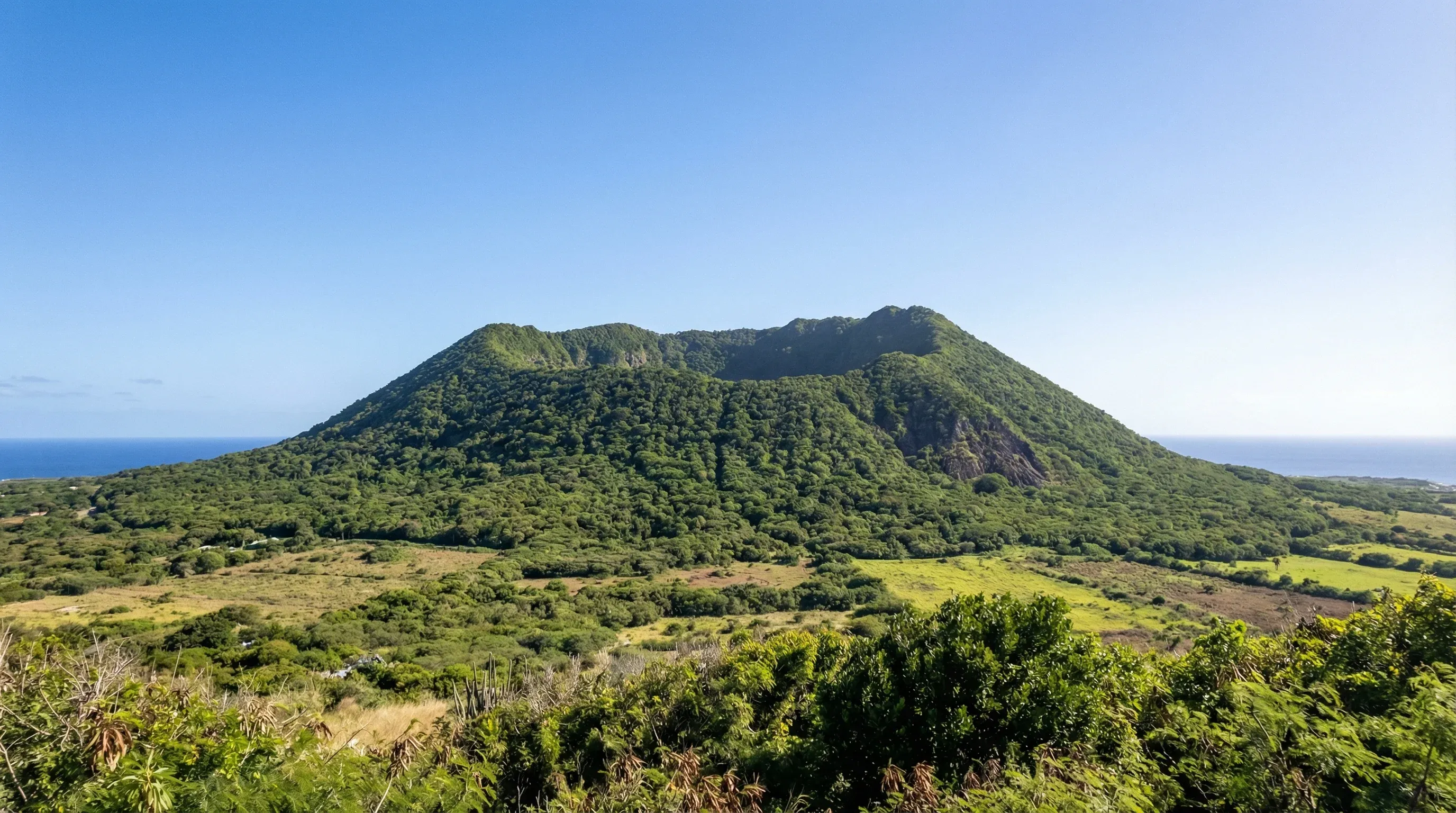 The symmetrical green slopes and crater rim of The Quill volcano on Sint Eustatius under a bright midday sky.