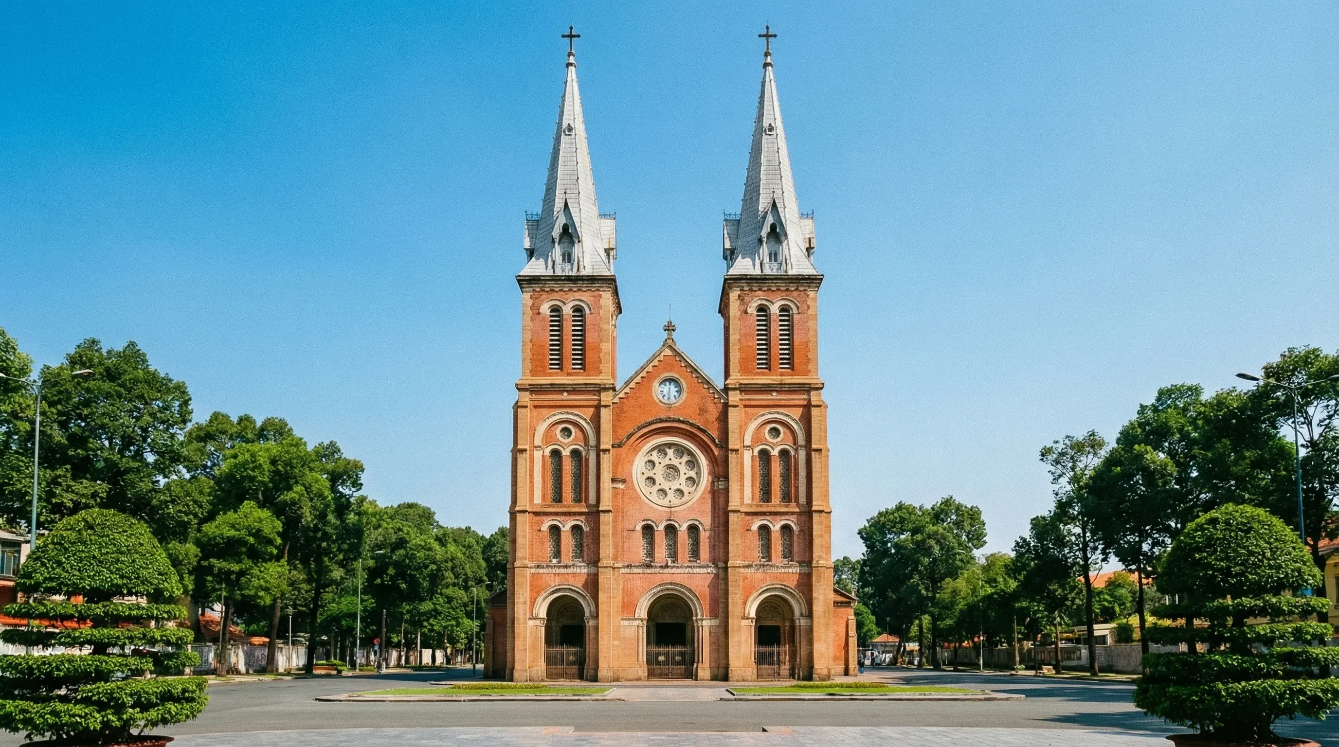 The red brick facade and twin bell towers of the Notre-Dame Cathedral Basilica of Saigon under a clear blue sky in Ho Chi Minh City.