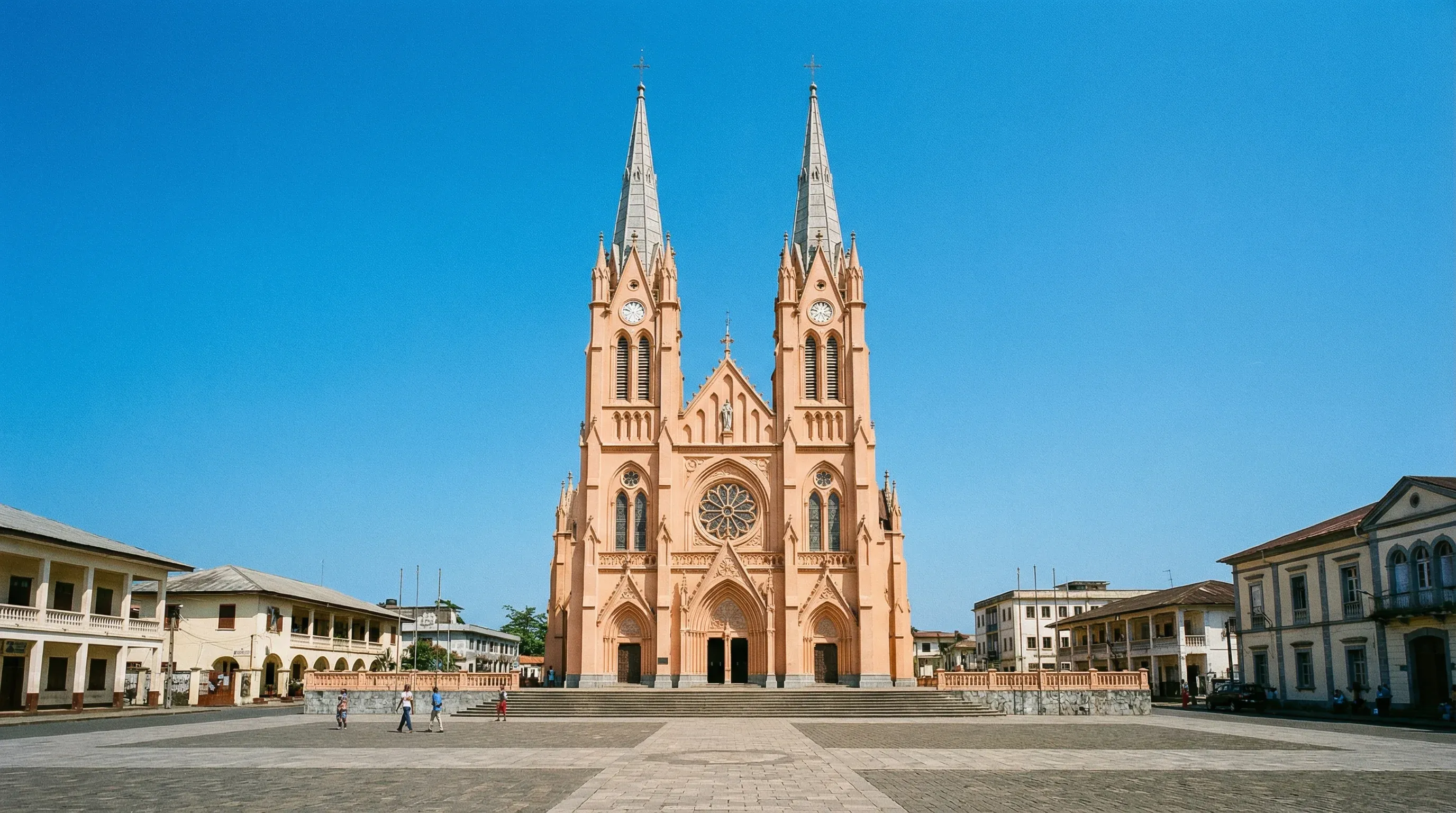 The Gothic Revival Saint Elizabeth's Cathedral in Malabo, featuring two prominent spires and a peach-colored exterior under a bright sun.