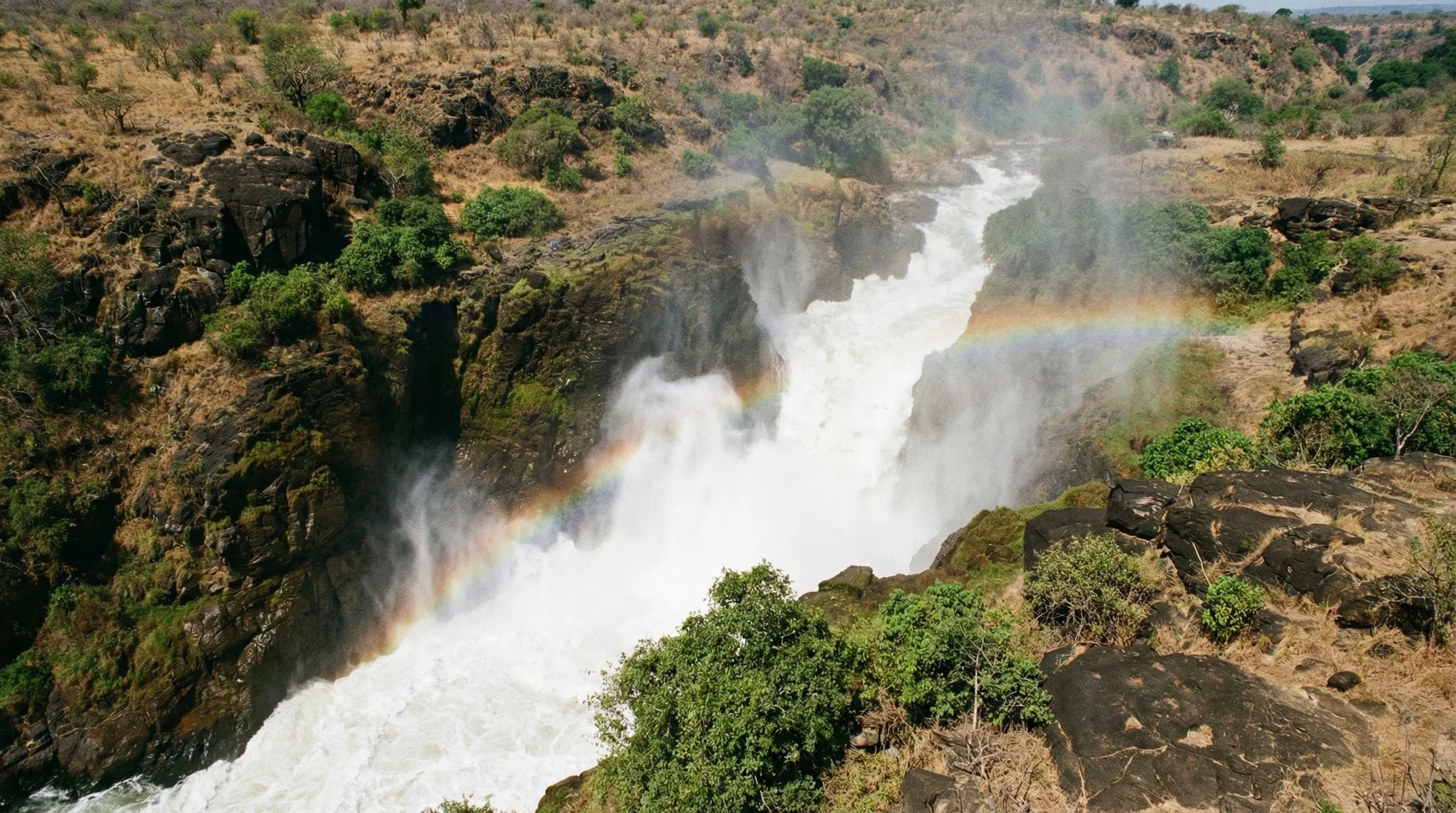 The Victoria Nile river squeezing through a narrow rocky gap at Murchison Falls, creating a powerful white waterfall and mist.