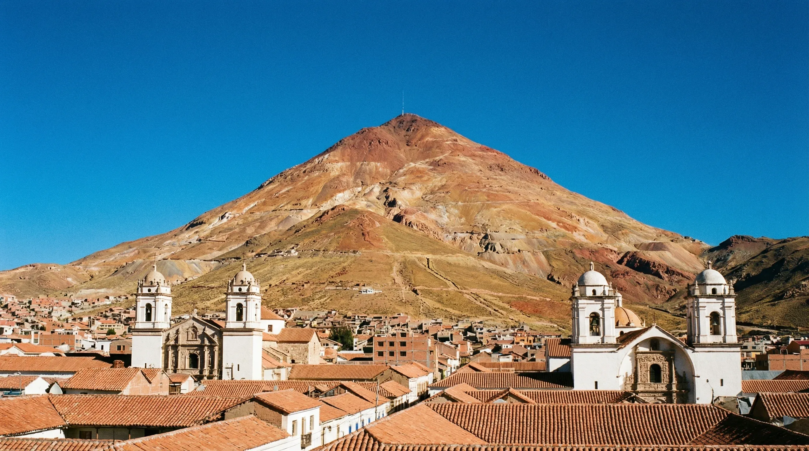 A large reddish conical mountain towering over a historic city with white buildings and red-tiled roofs.