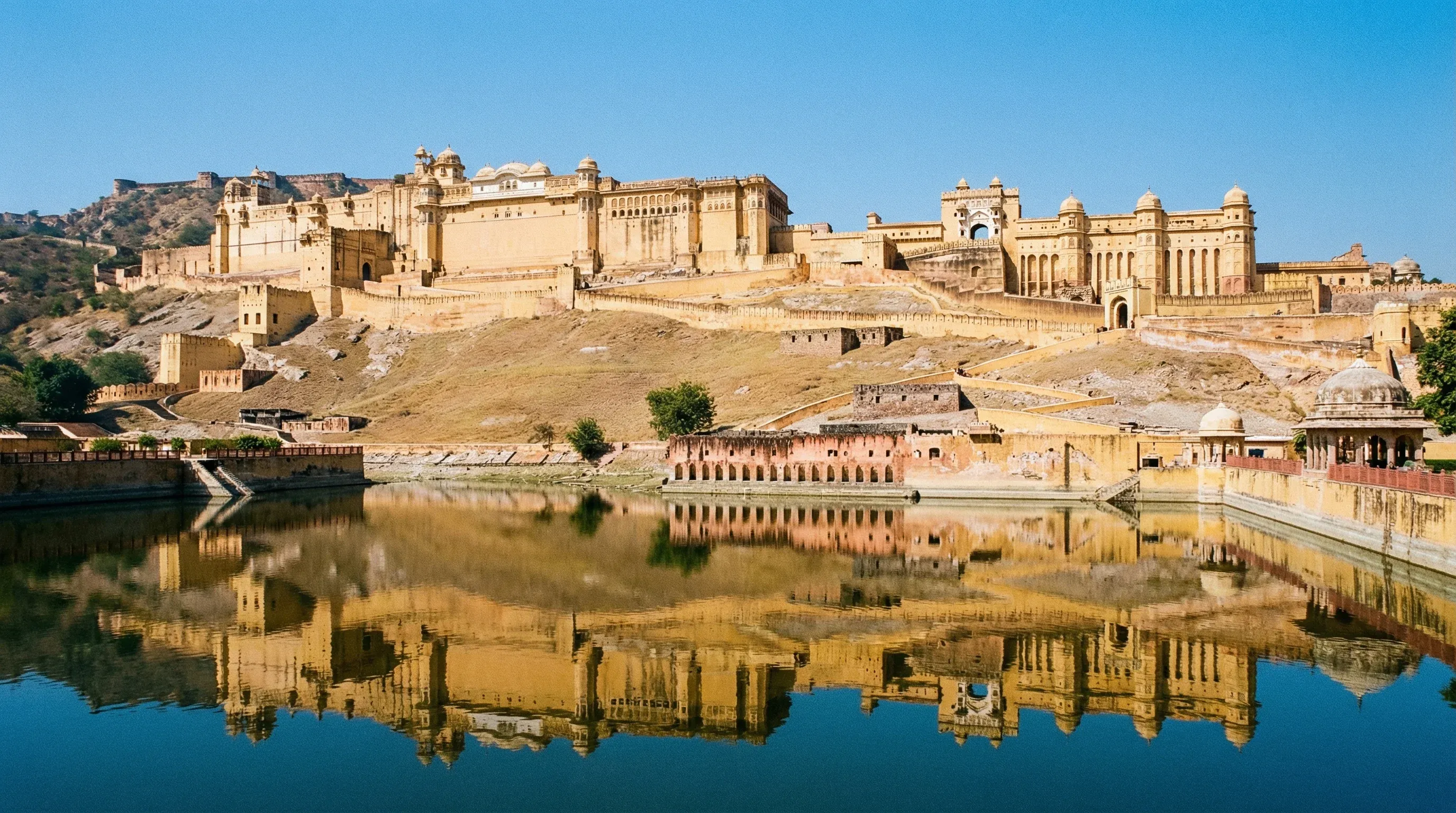 Amer Fort in Jaipur, Rajasthan, viewed from across Maota Lake under a clear sky.