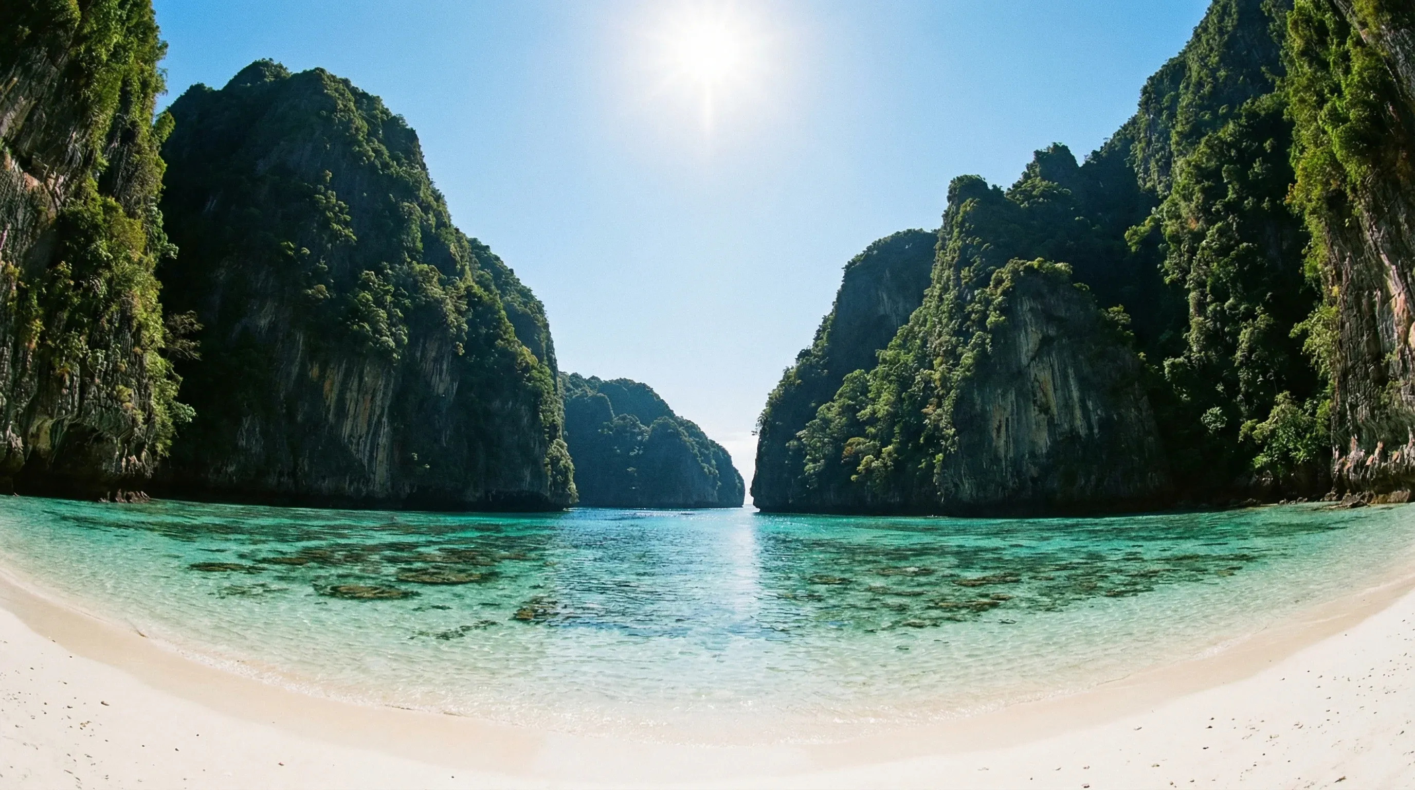 A white sand beach at Maya Bay on Ko Phi Phi Le, framed by high limestone cliffs and turquoise water under a clear sky.