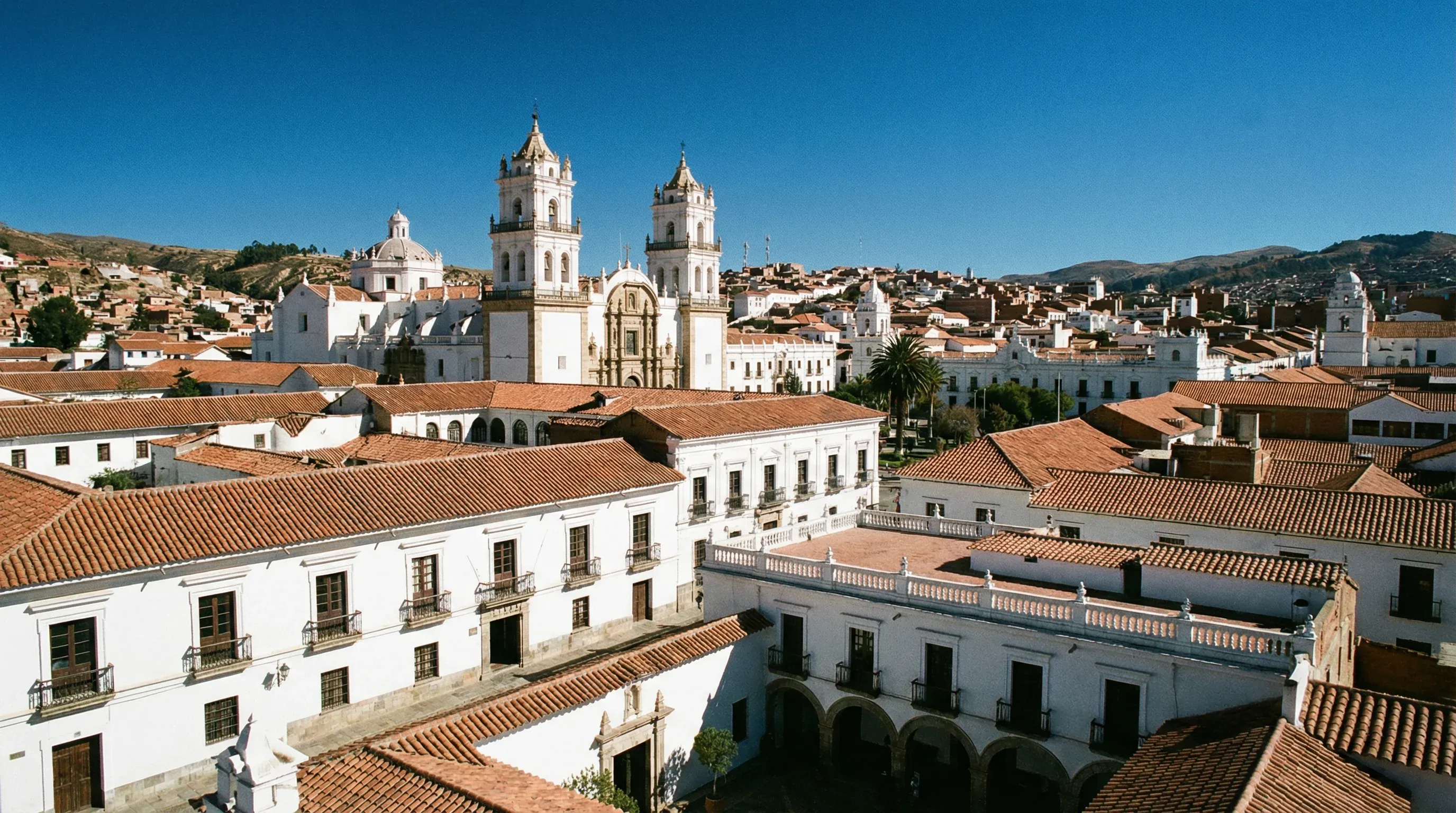 A view of whitewashed colonial buildings and a grand cathedral tower under a bright blue sky.