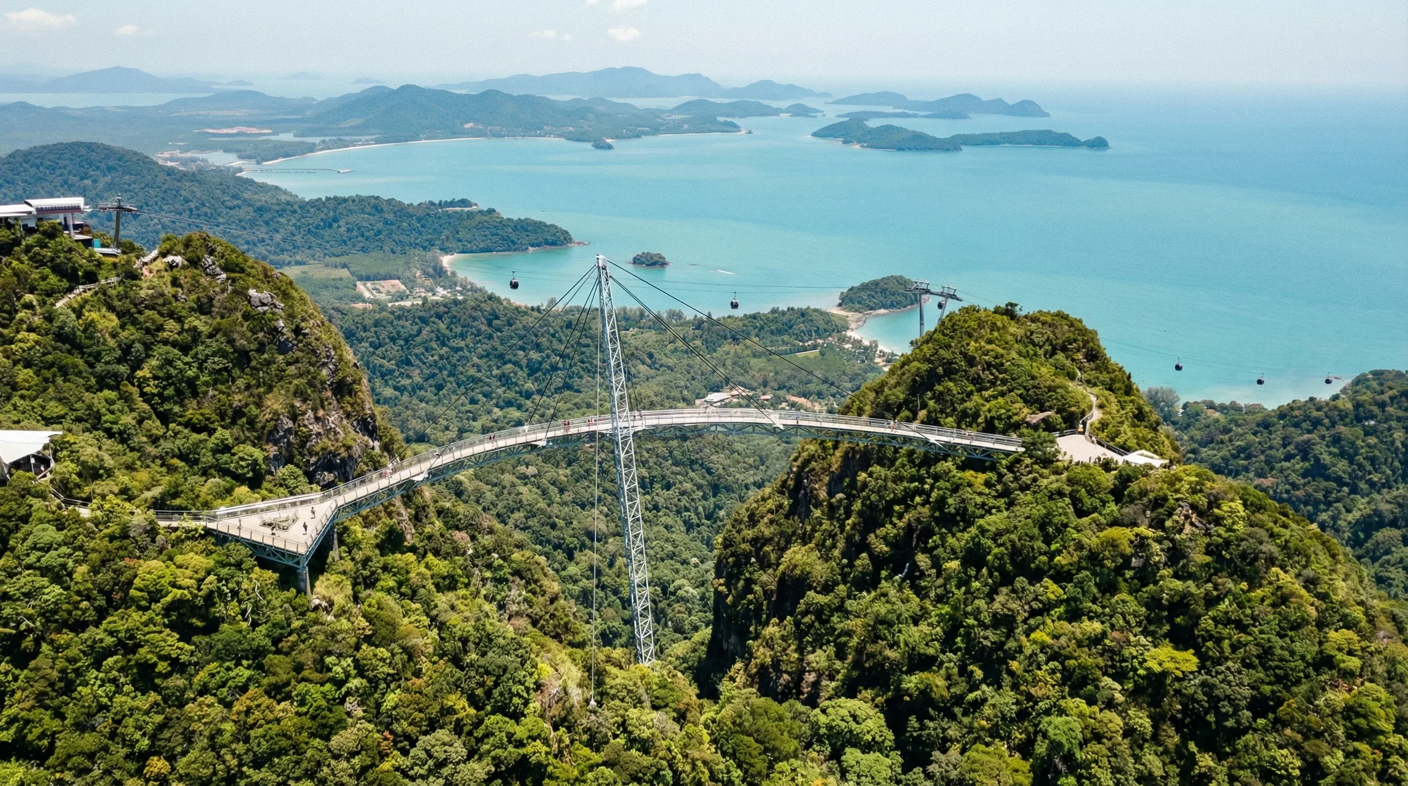 A curved steel pedestrian bridge suspended between mountain peaks overlooking the forested islands and turquoise sea of Langkawi.