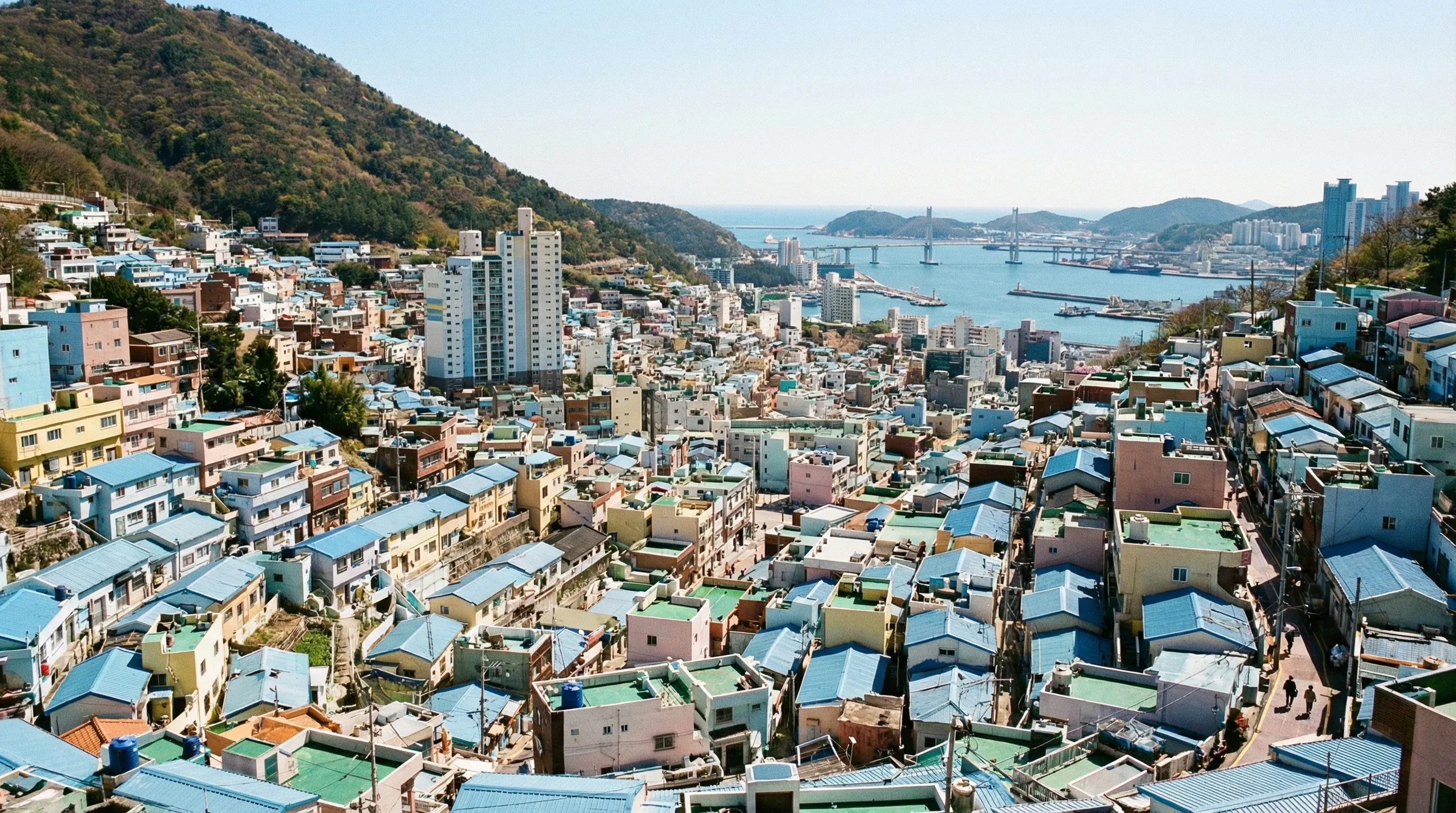 A wide view of colorful houses terraced on a hillside in Gamcheon Culture Village, Busan, with the sea in the background.