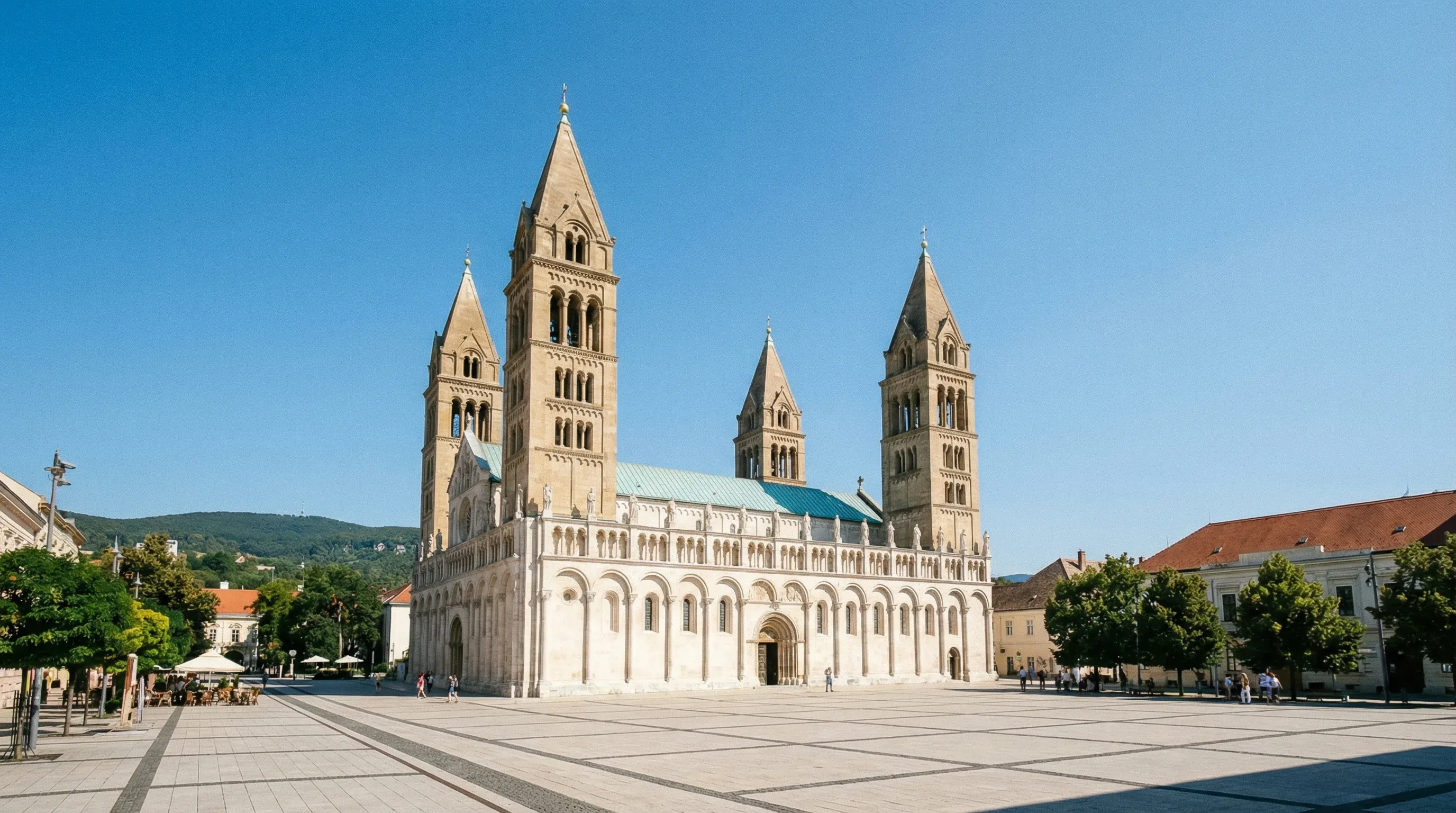The four-towered stone cathedral of Pécs standing in a paved square under a bright, clear sky.
