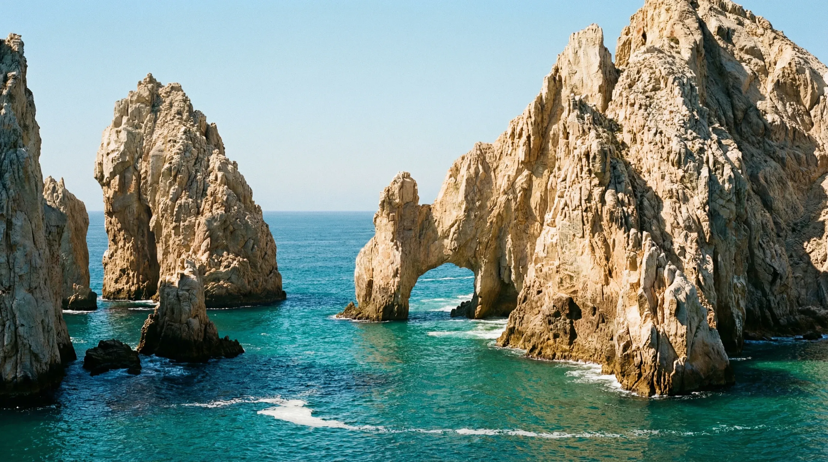 A natural granite sea arch stands in turquoise water under a clear blue sky at the tip of the Baja Peninsula.