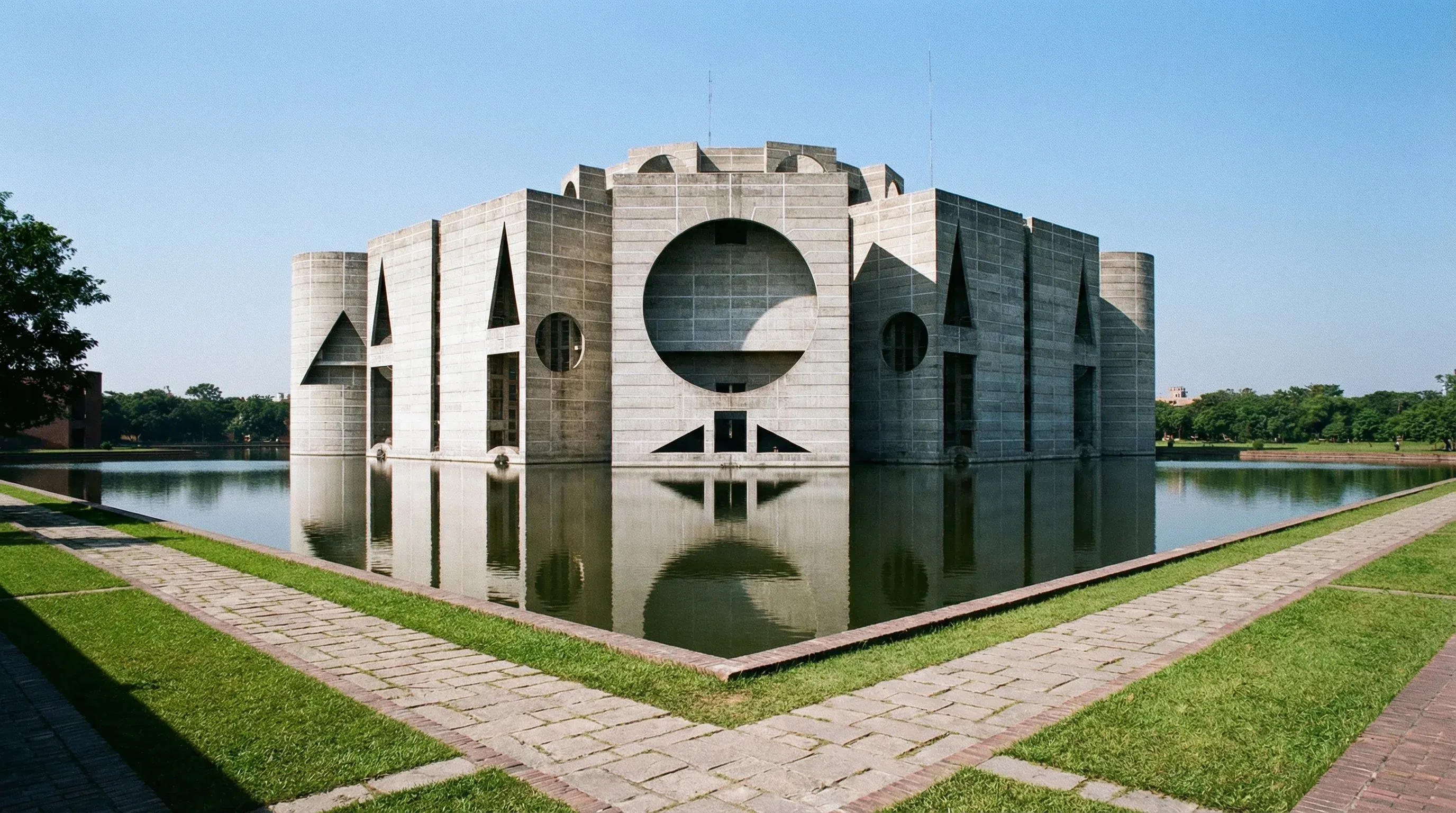 The geometric concrete architecture of the National Parliament House in Dhaka, reflected in the surrounding water.