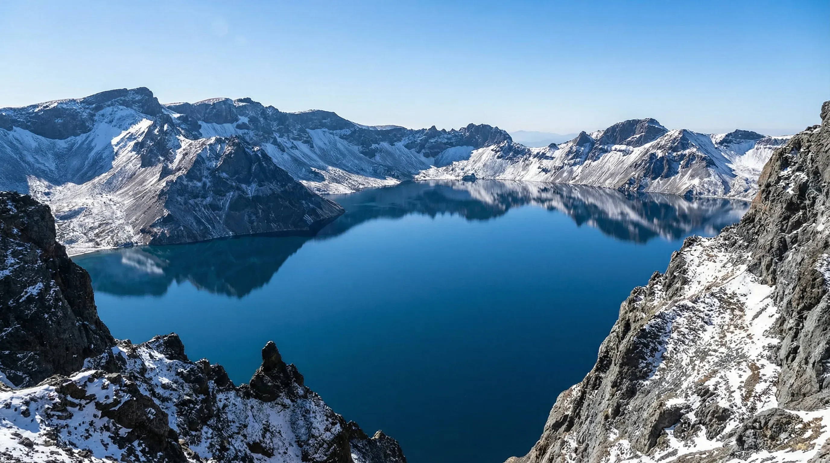 A deep blue crater lake surrounded by steep, rocky mountain peaks at the summit of Changbai Mountain.