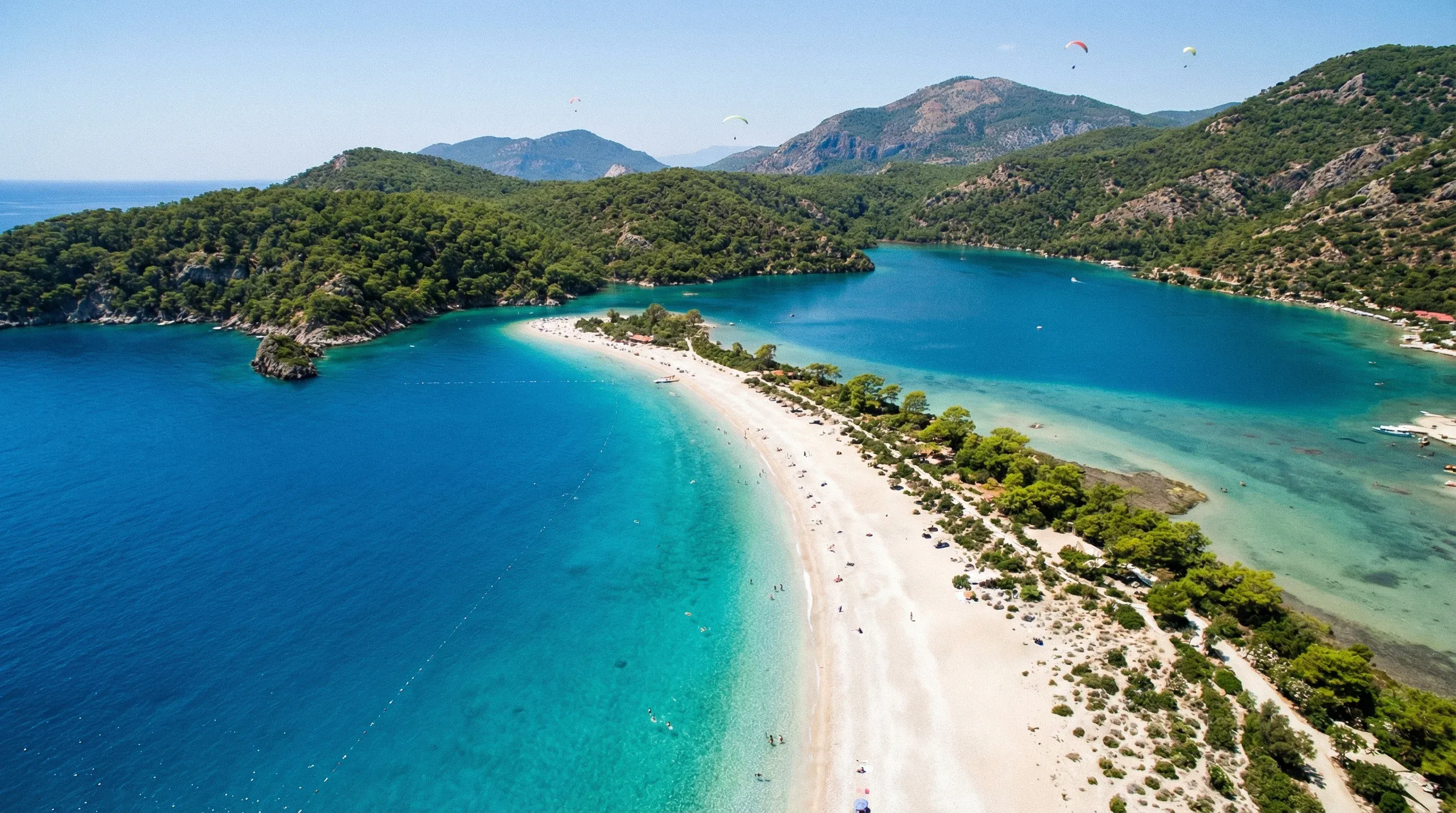 A high-angle view of a white sand spit and turquoise lagoon water surrounded by green mountains in Ölüdeniz.