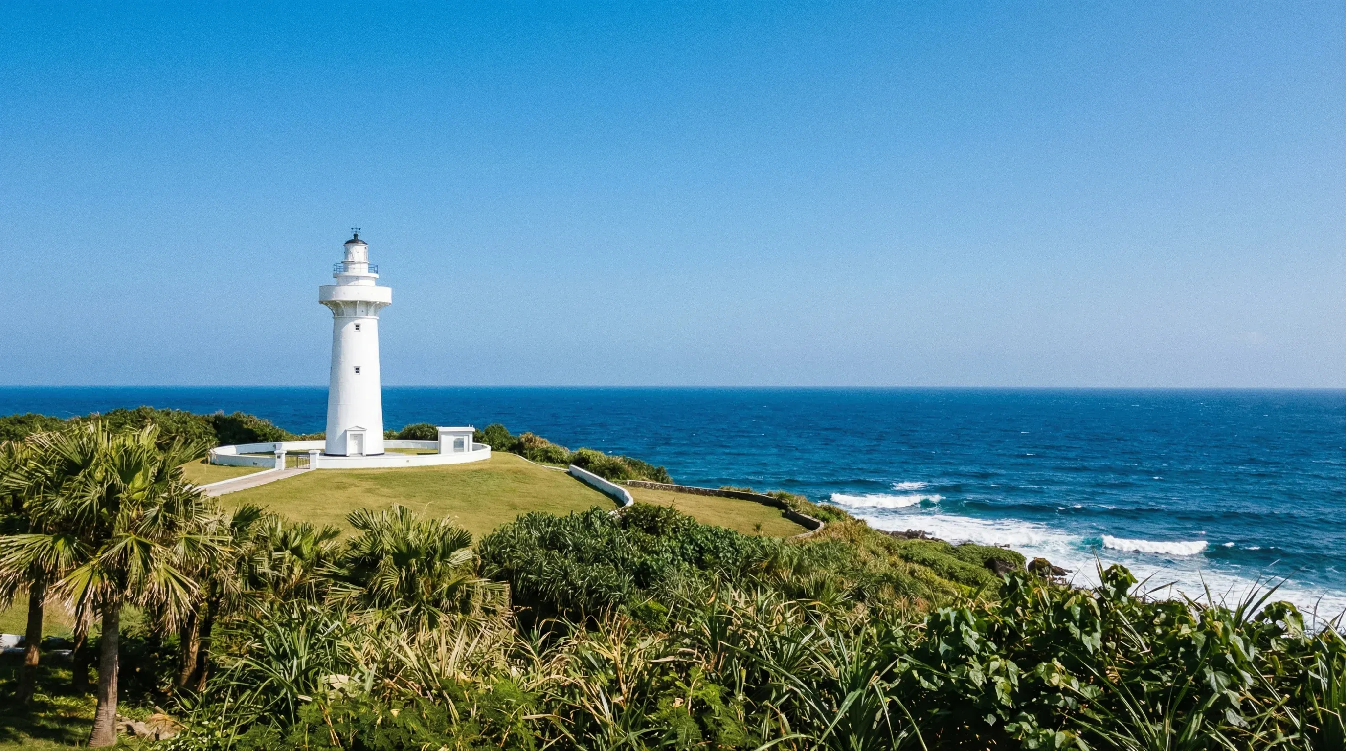 The white Eluanbi Lighthouse standing on a green hill overlooking the ocean in Kenting National Park.