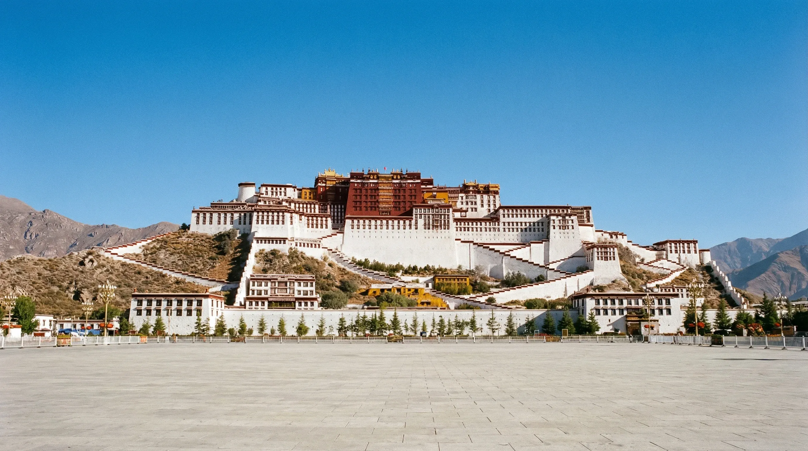 The massive red and white Potala Palace architectural complex on a hill under a clear blue sky.