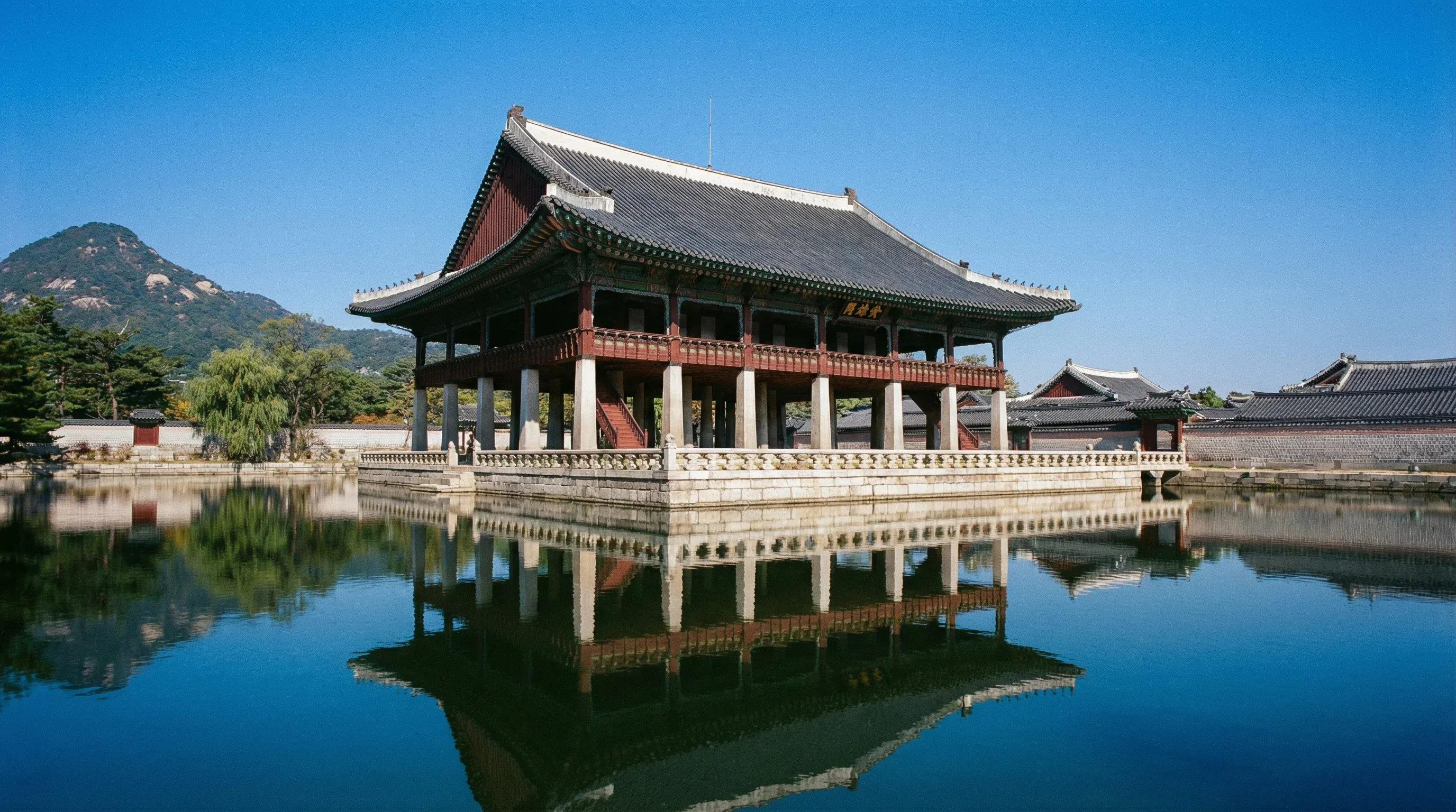 The Gyeonghoeru Pavilion reflecting in a still pond at Gyeongbokgung Palace in Seoul with mountains in the background.