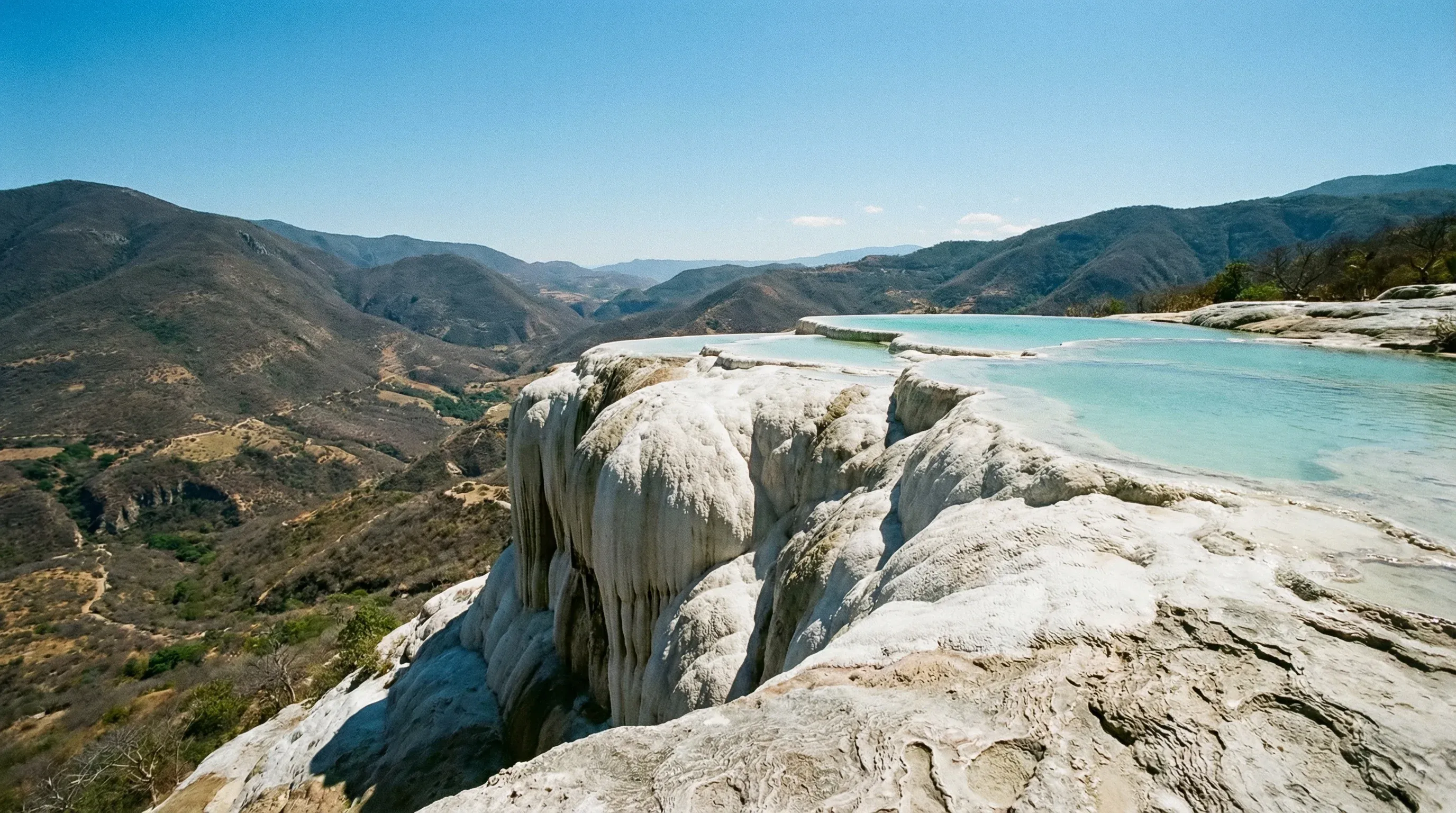 White petrified mineral waterfalls and turquoise pools overlook a vast mountain valley in Oaxaca.
