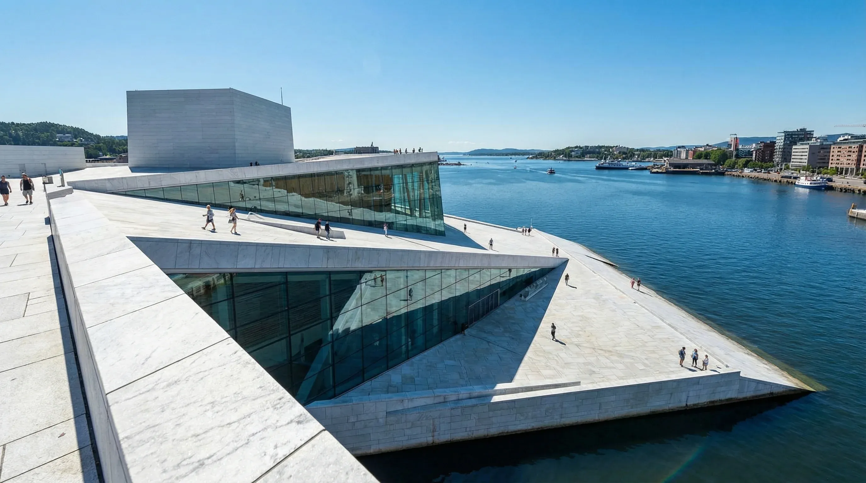 The angular white marble and glass Oslo Opera House building sloping into the blue water of the Oslofjord.