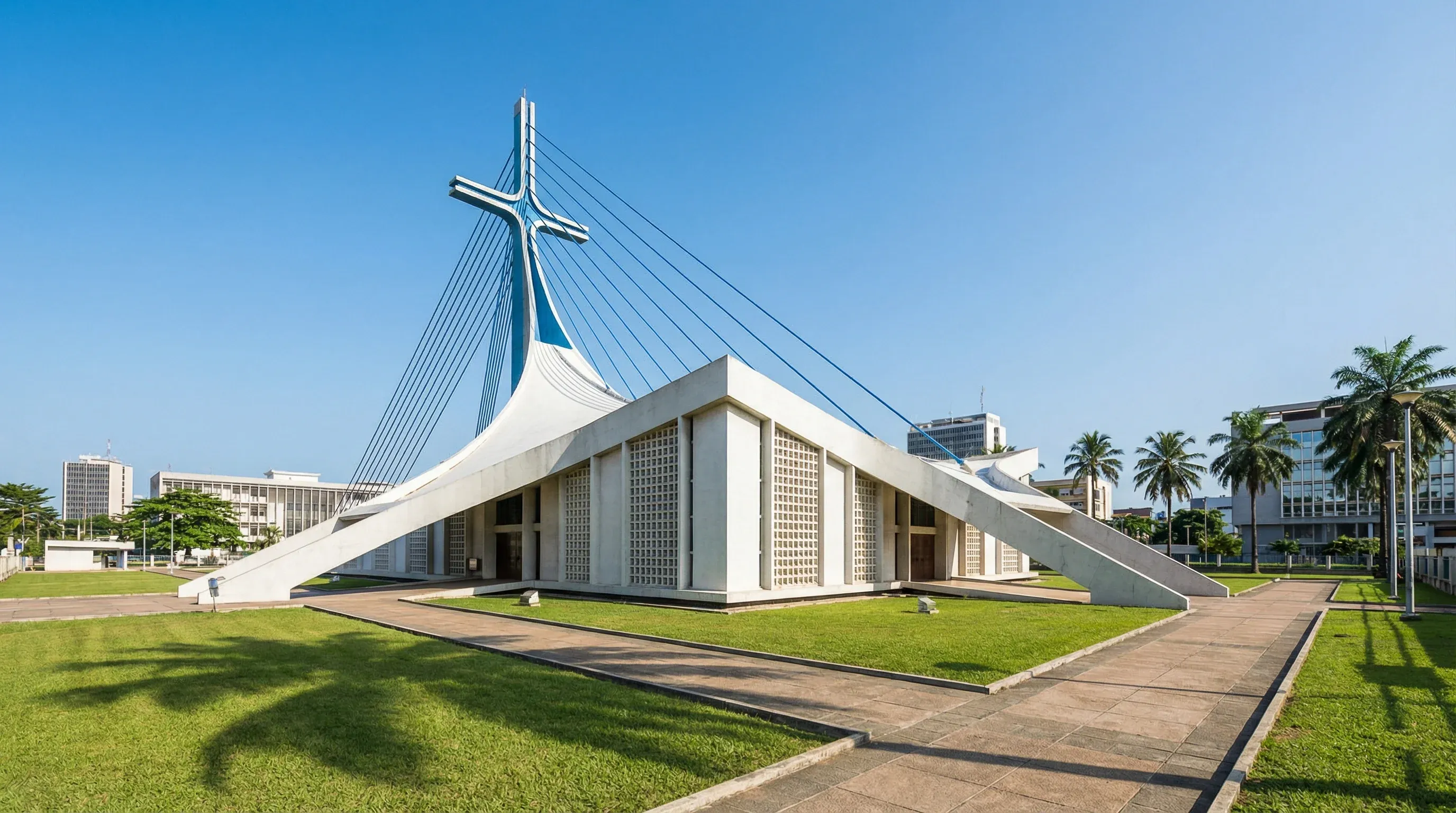 The modernist white concrete St. Paul's Cathedral in Abidjan with its blue cable-stayed cross under a clear blue sky.