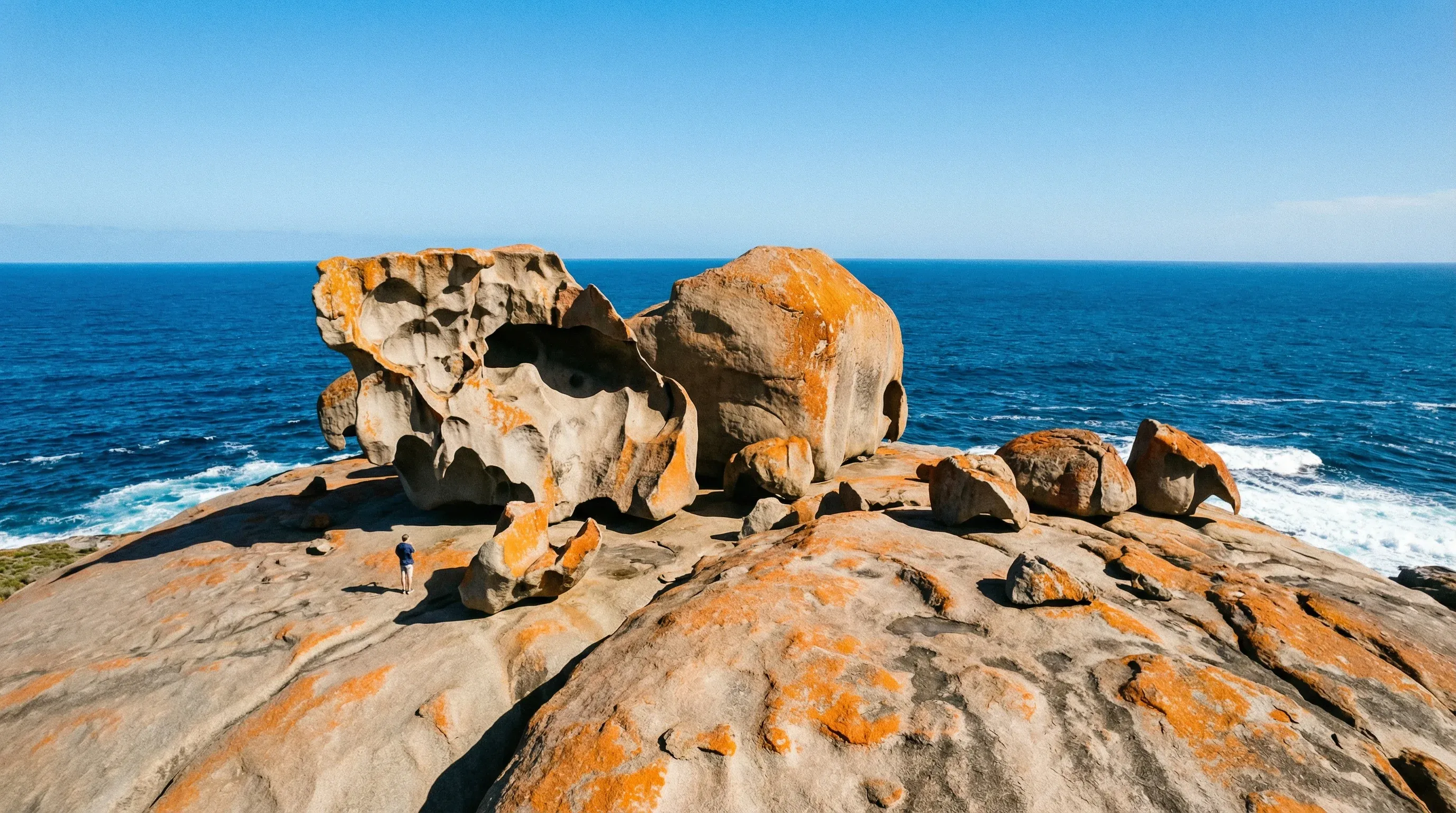 Large orange-lichen-covered granite boulders on a coastal cliff overlooking the Southern Ocean at Remarkable Rocks.