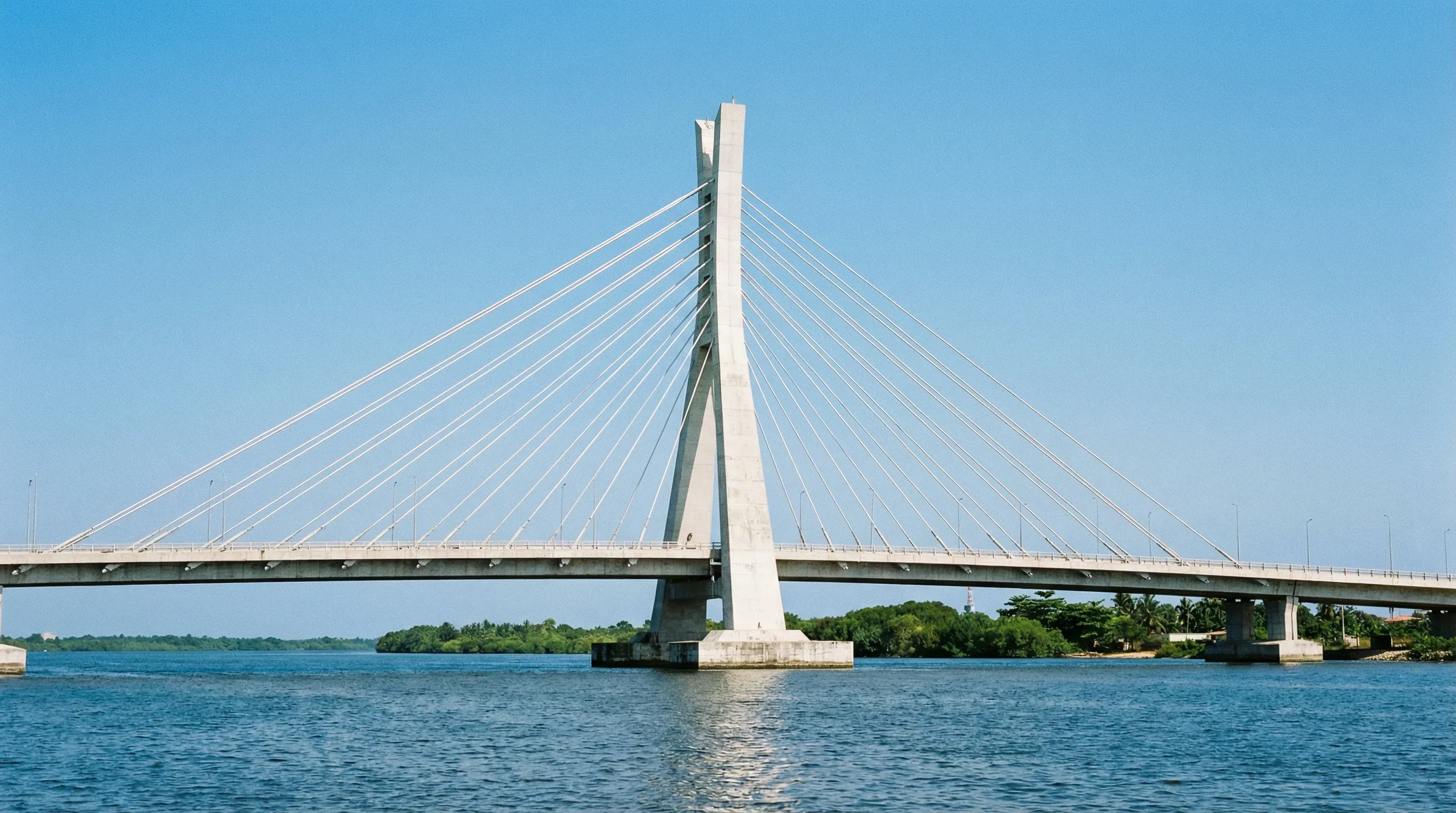 The white cable-stayed Lekki-Ikoyi Link Bridge spans across the blue water of the Lagos lagoon under a bright sun.