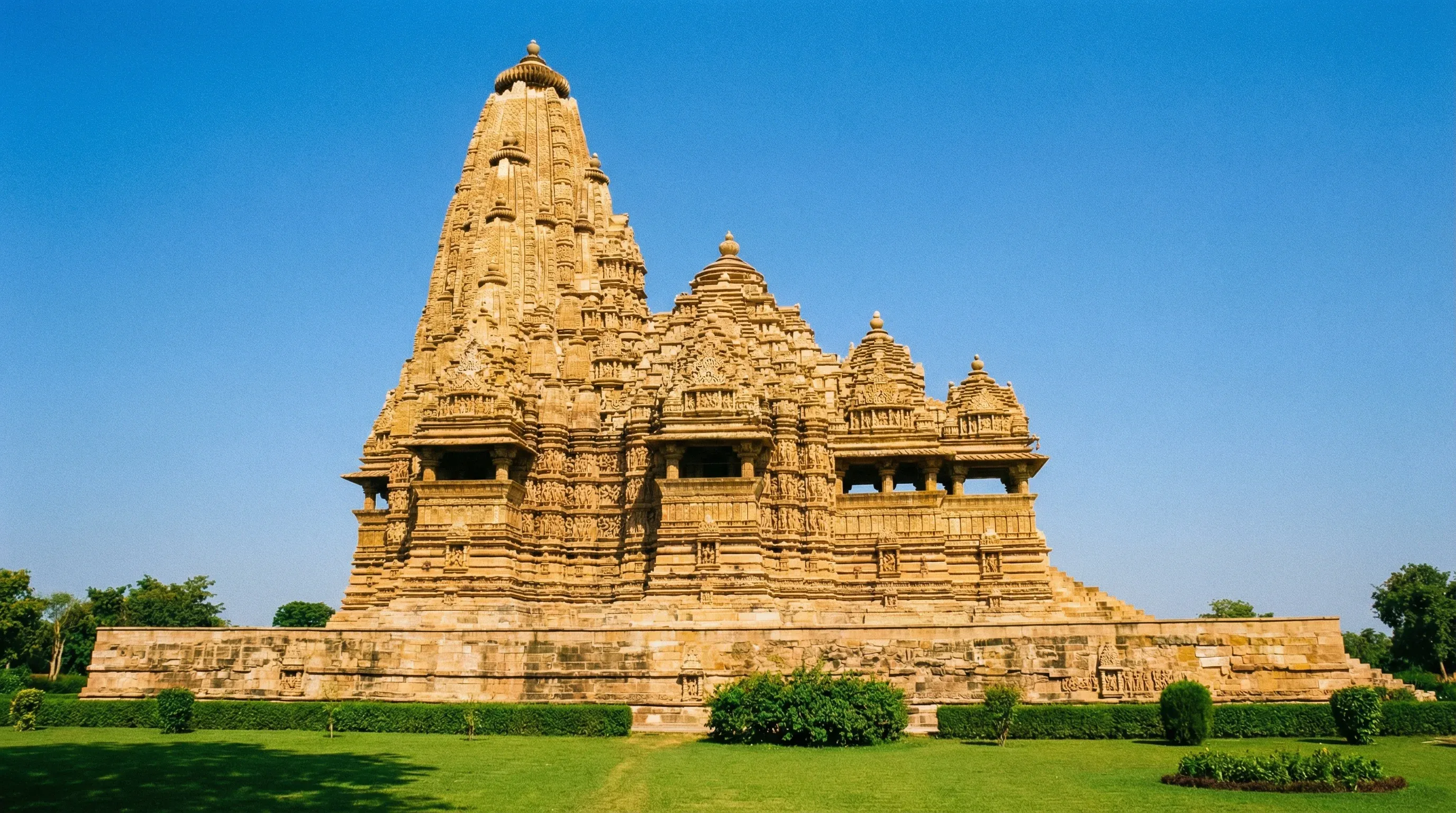 The Kandariya Mahadeva Temple in Khajuraho, showing detailed sandstone architecture against a clear blue sky.