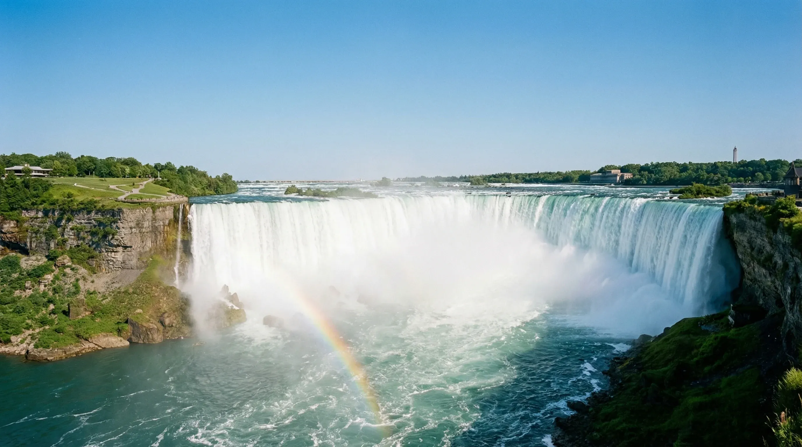 A wide-angle view of the Horseshoe Falls in Niagara Falls, Ontario, with mist rising from the bottom and a rainbow visible in the spray.
