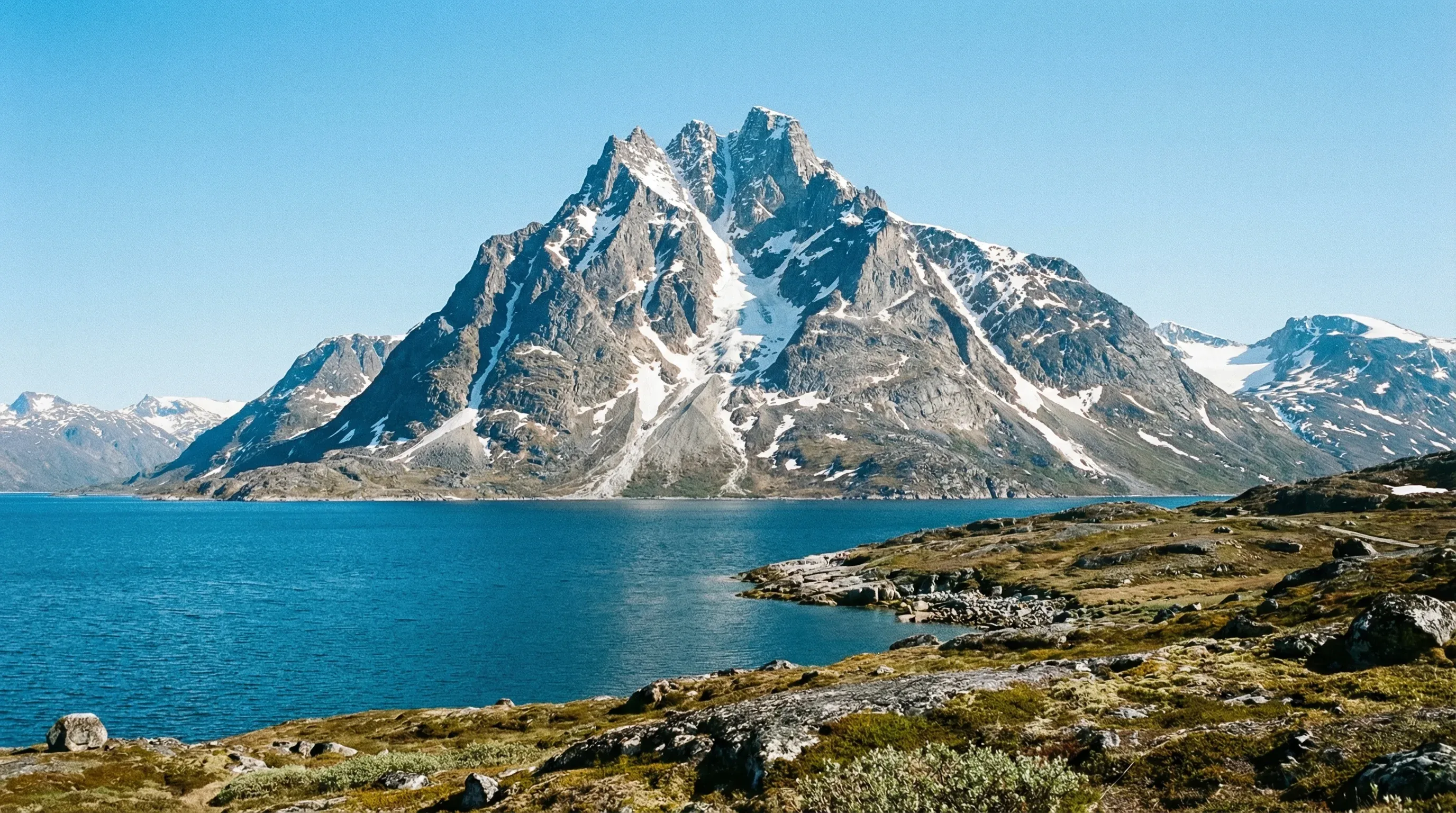 The jagged peak of Sermitsiaq Mountain standing behind the deep blue waters of the Nuuk Fjord system in Southwest Greenland.