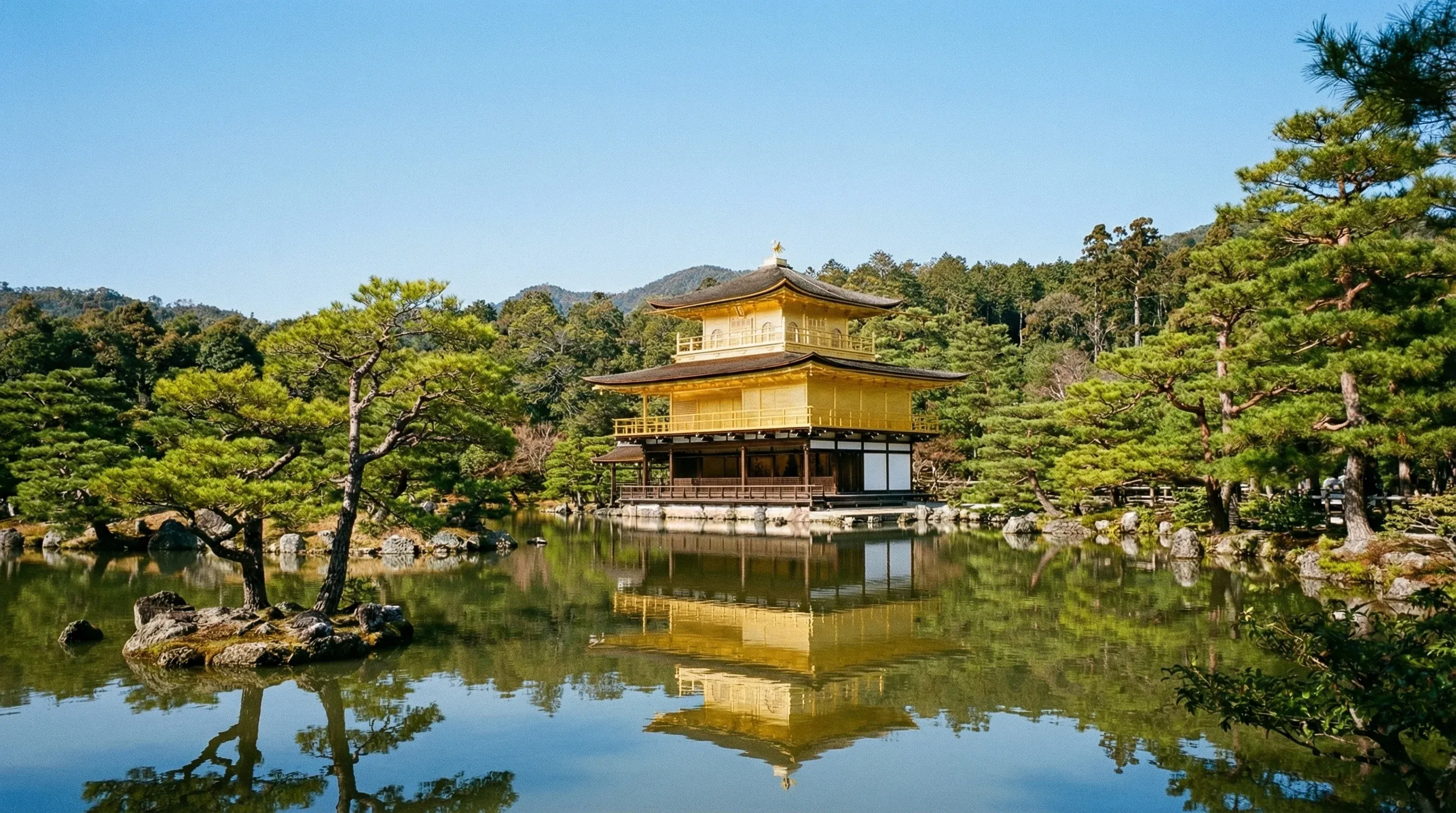 The gold-covered Kinkaku-ji temple reflected in a calm pond surrounded by pine trees in Kyoto.