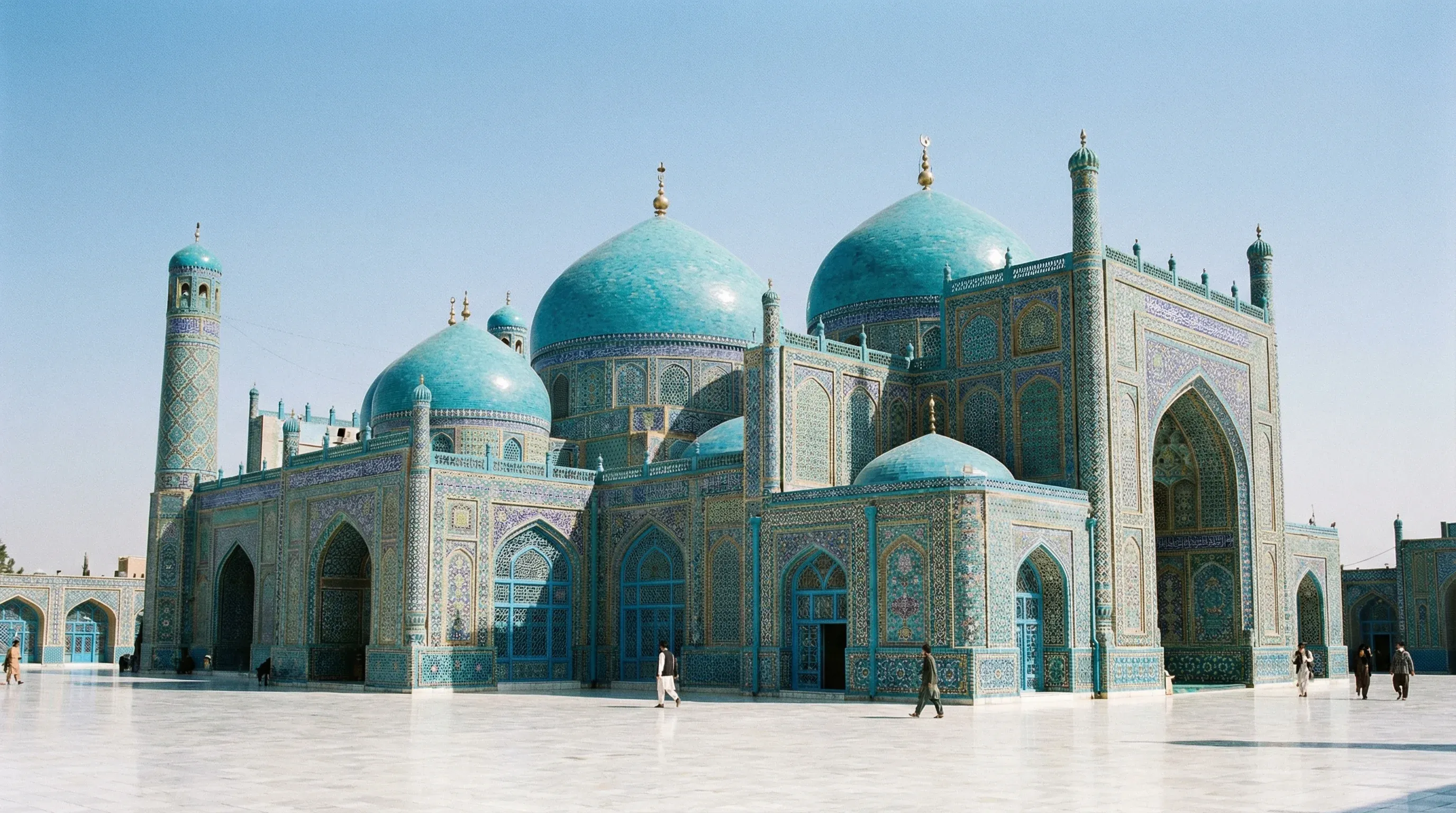 The ornate Blue Mosque in Mazar-i-Sharif, decorated with vibrant blue tiles and domes on a white marble plaza.