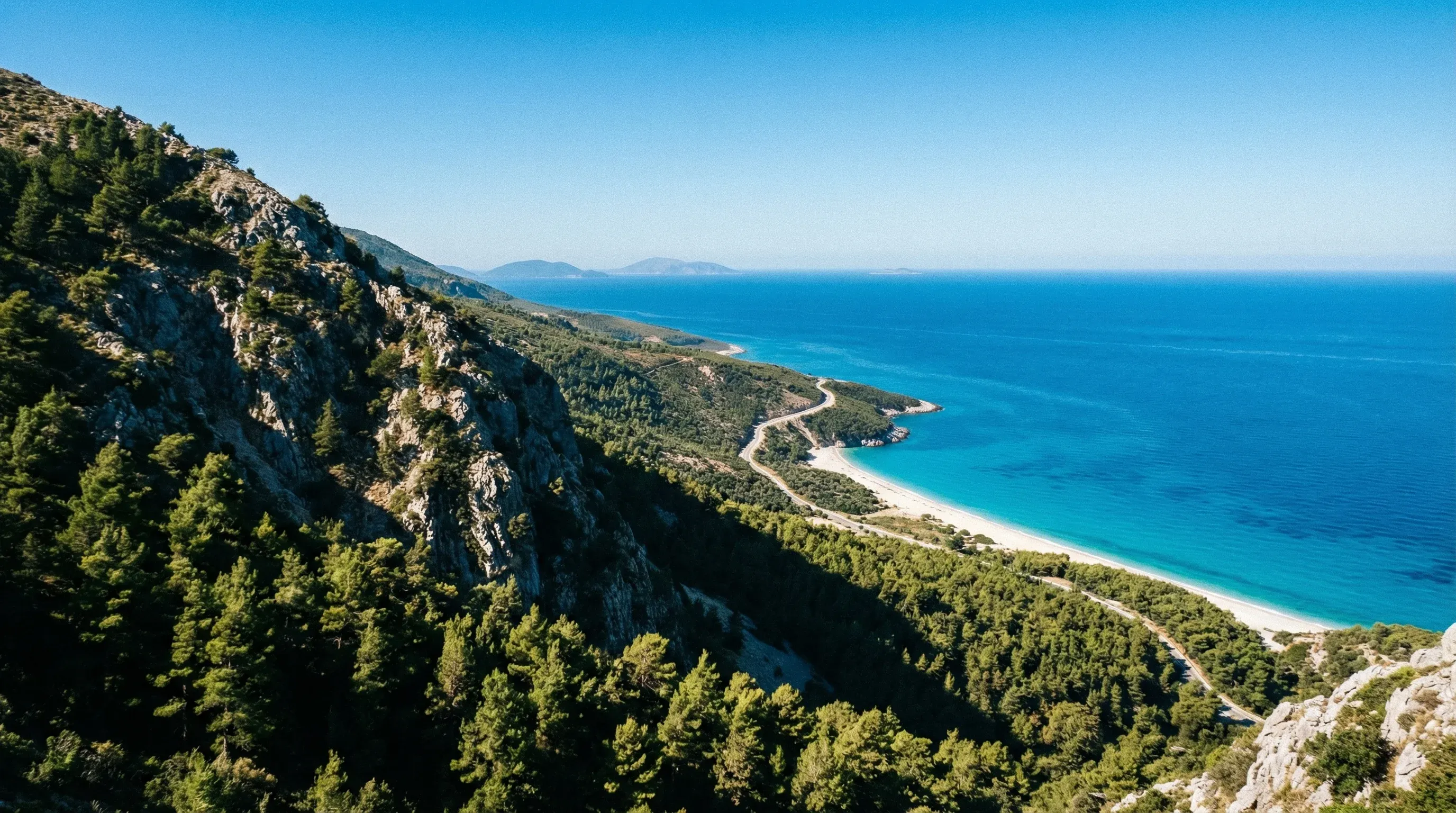 High-altitude panoramic view from Llogara Pass looking down at the turquoise Ionian Sea and the white pebble coastline of Palasa.