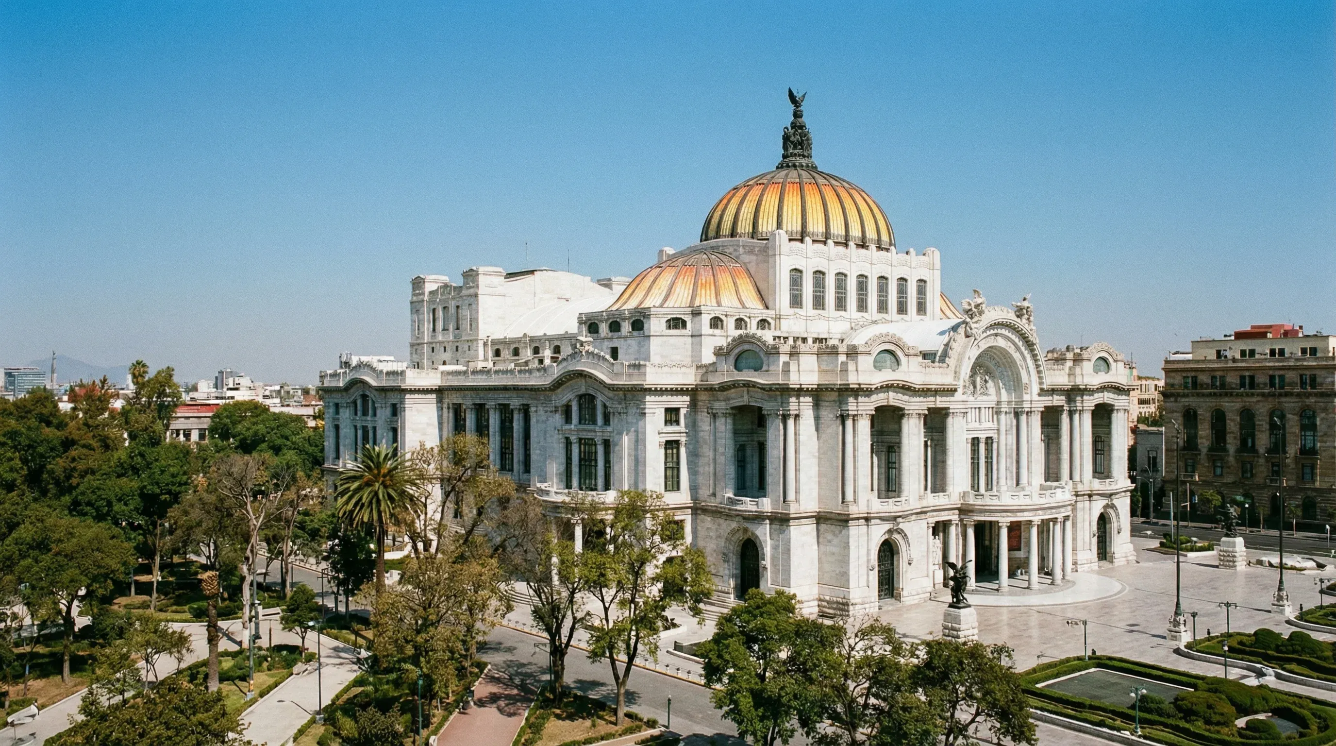 The white marble Palacio de Bellas Artes with its yellow and orange tiled dome in Mexico City under a blue sky.
