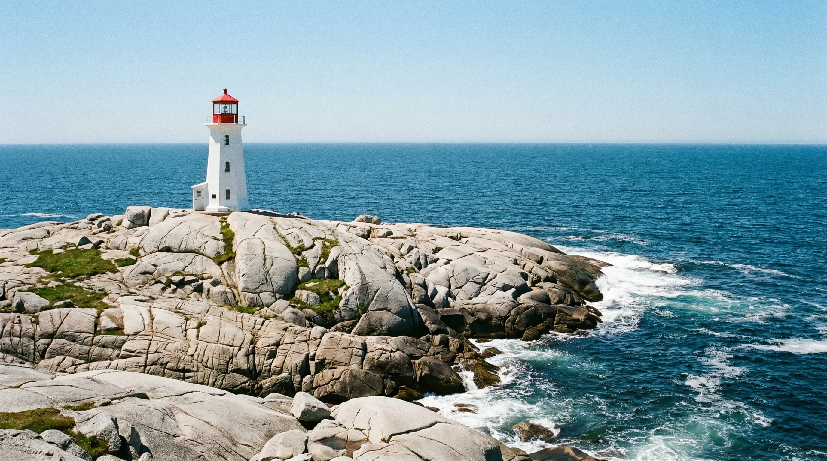 The Peggy's Point Lighthouse standing on grey granite rocks beside the Atlantic Ocean in Nova Scotia.