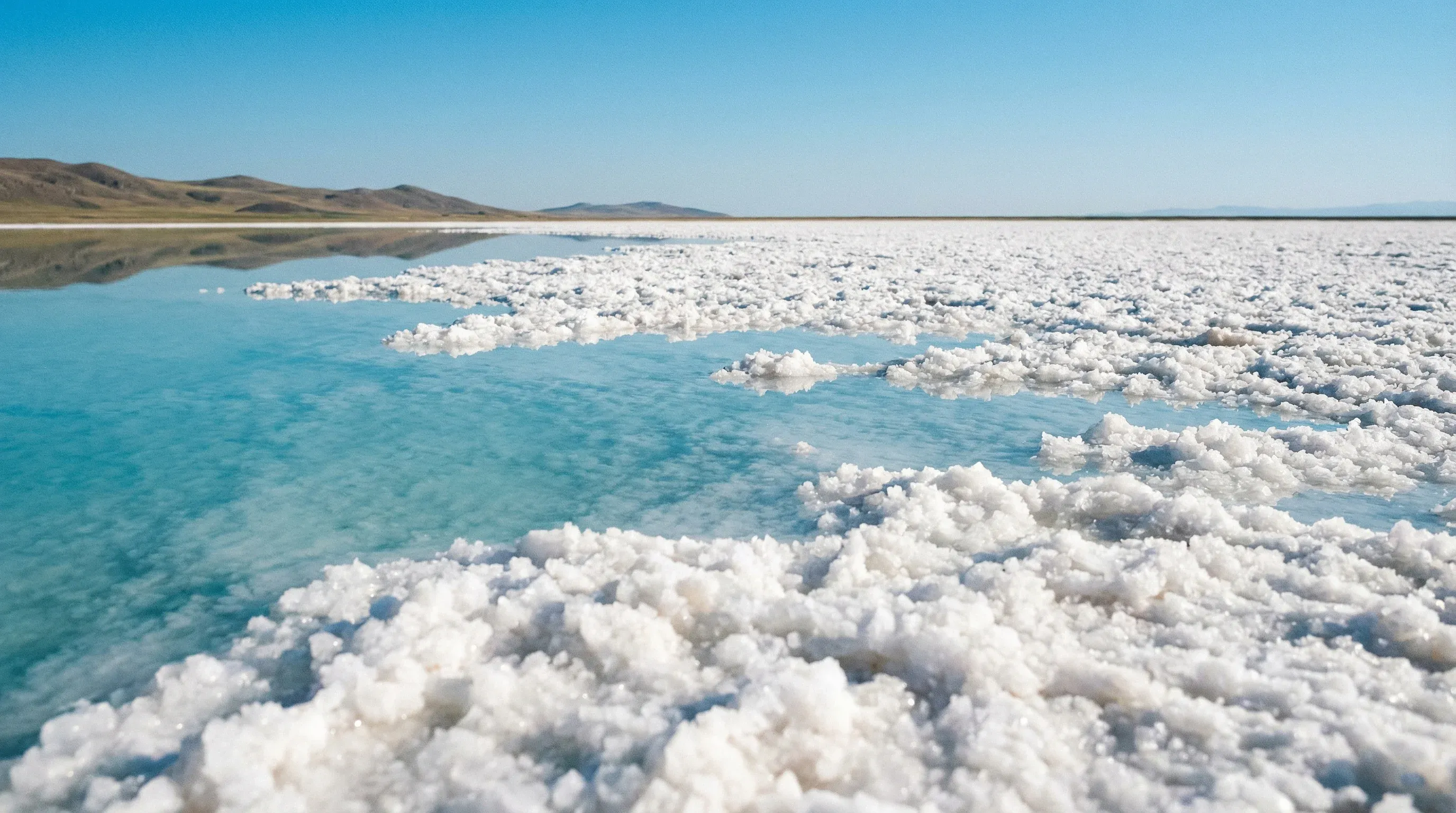 A vast white salt flat with a shallow layer of reflective water under a bright blue sky at Tuz Gölü.