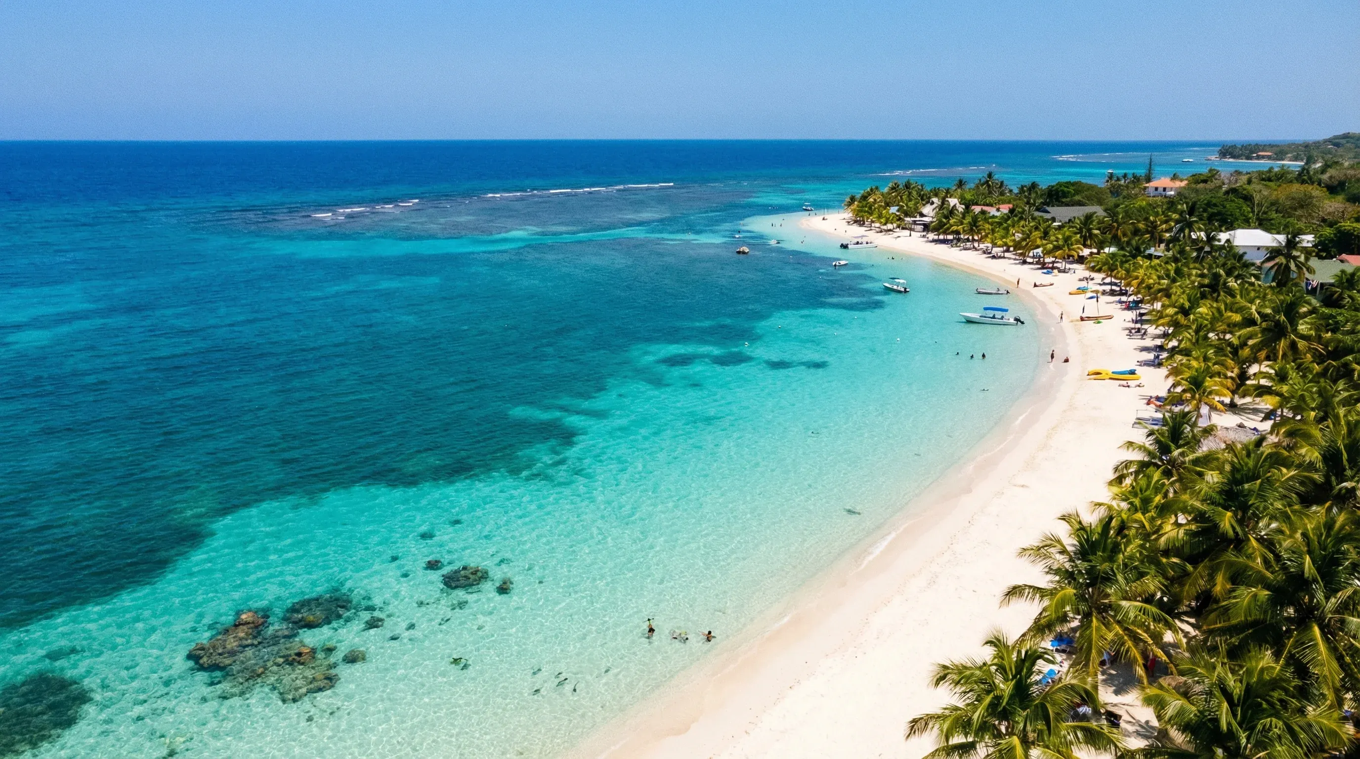 An aerial-style view of a white sand beach and turquoise Caribbean water along the coast of Roatán.