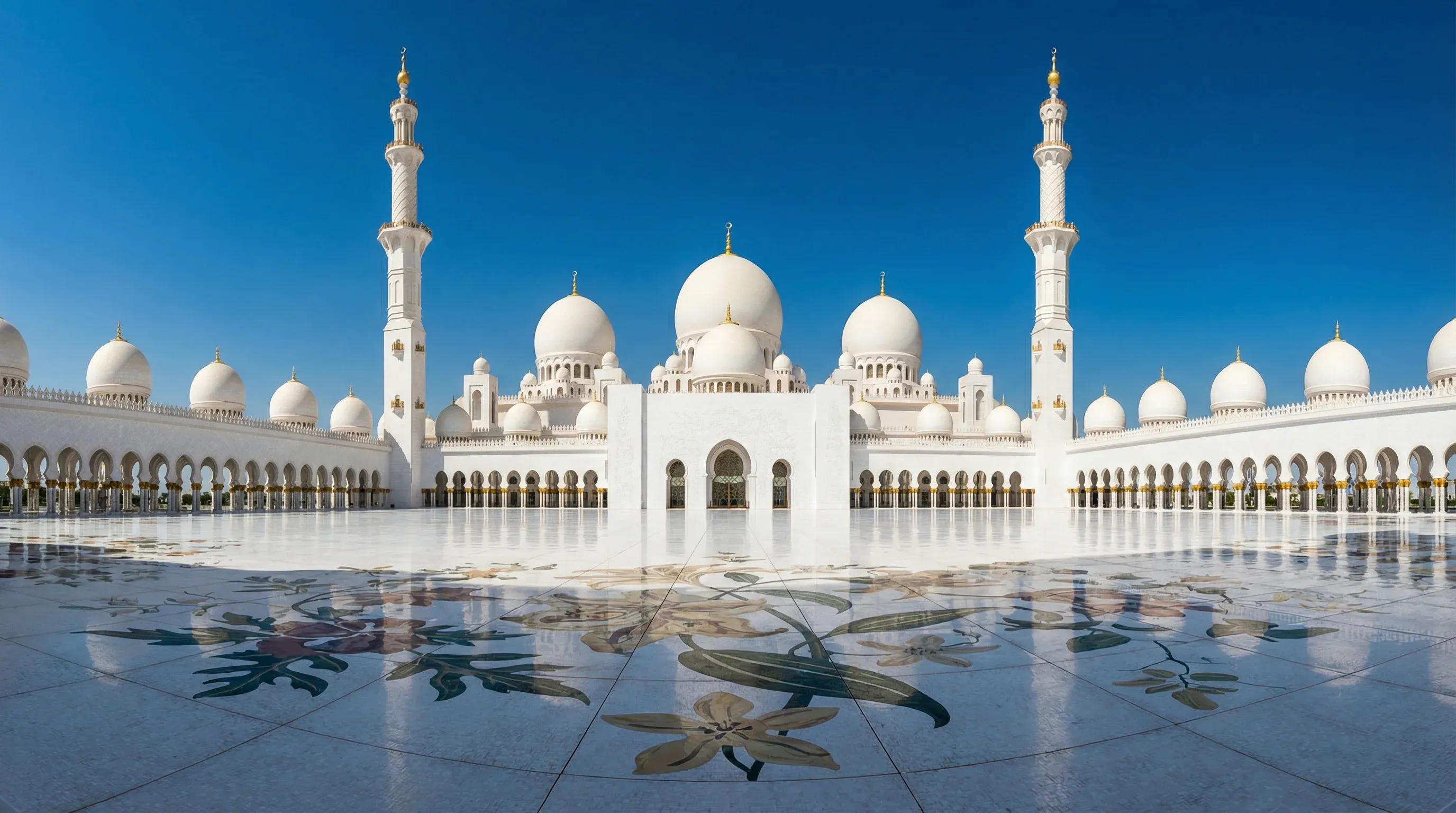 The white domes and minarets of the Sheikh Zayed Grand Mosque in Abu Dhabi under a clear blue sky.